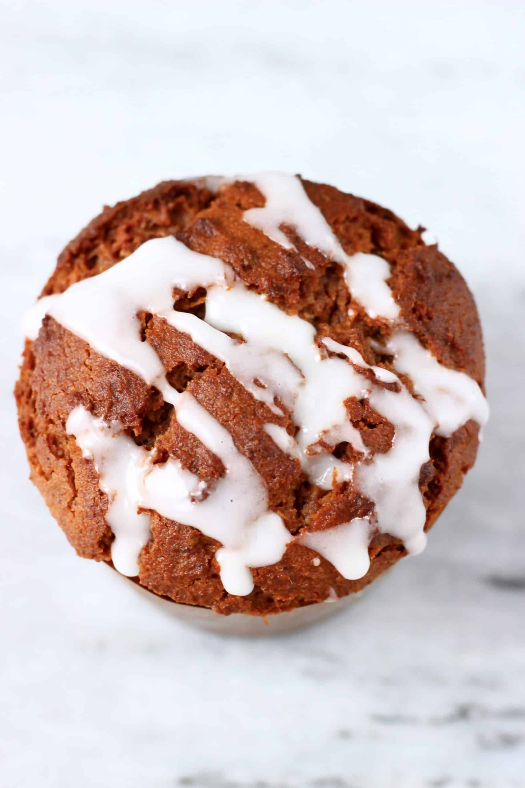 A gluten-free vegan gingerbread muffin in a brown muffin case drizzled with icing