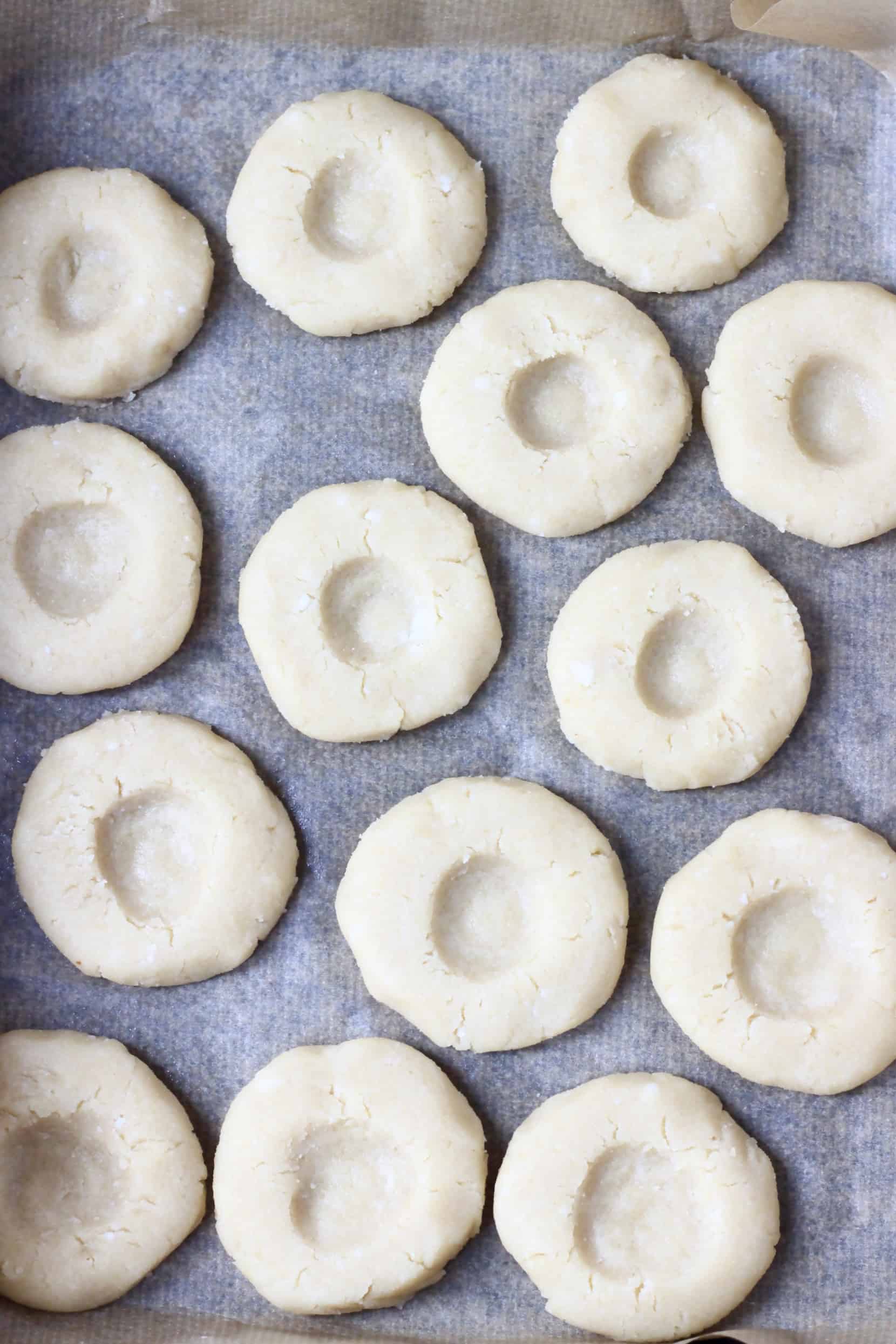 Raw gluten-free vegan thumbprint cookies with indents on a baking tray lined with baking paper