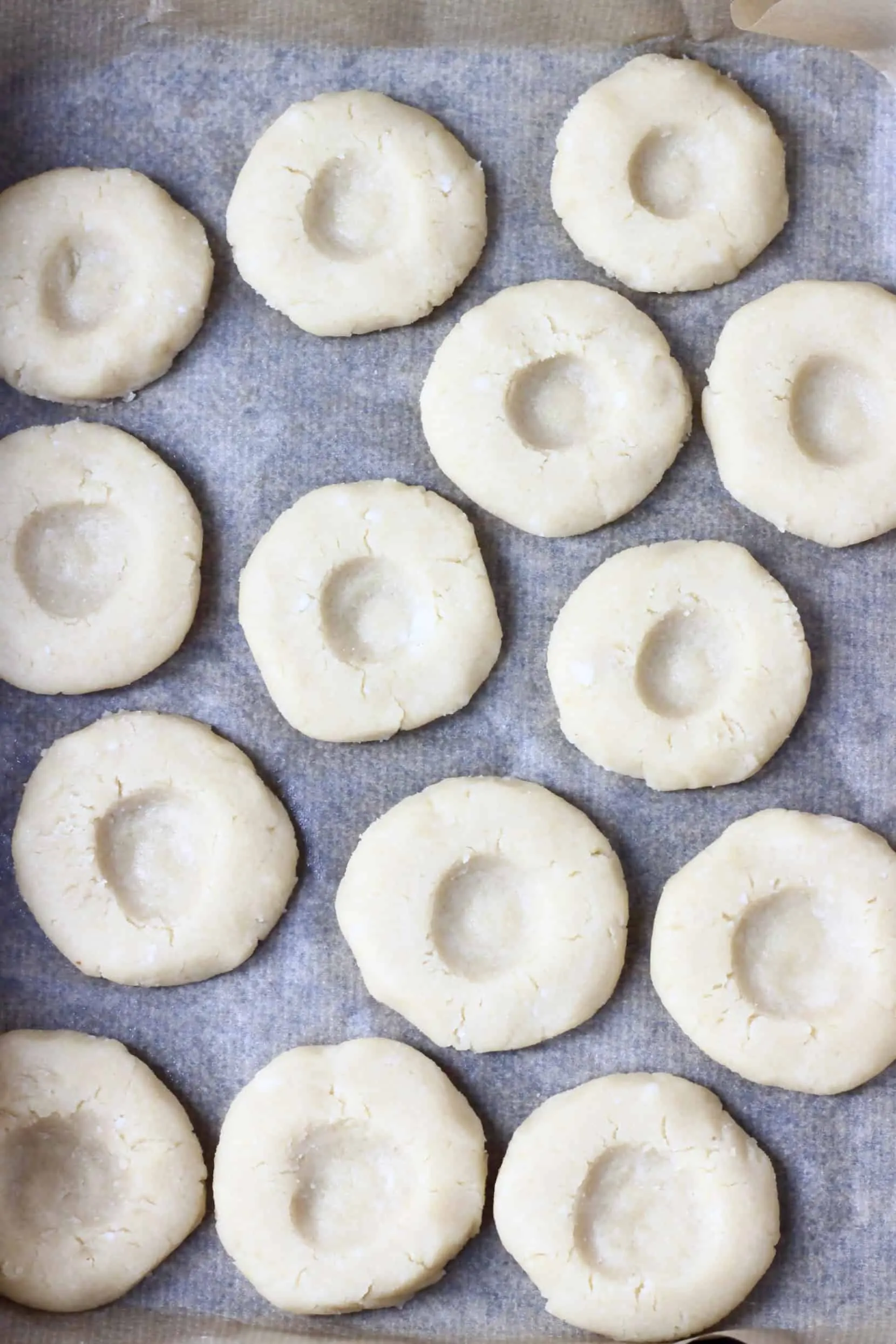 Raw gluten-free vegan thumbprint cookies with indents on a baking tray lined with baking paper