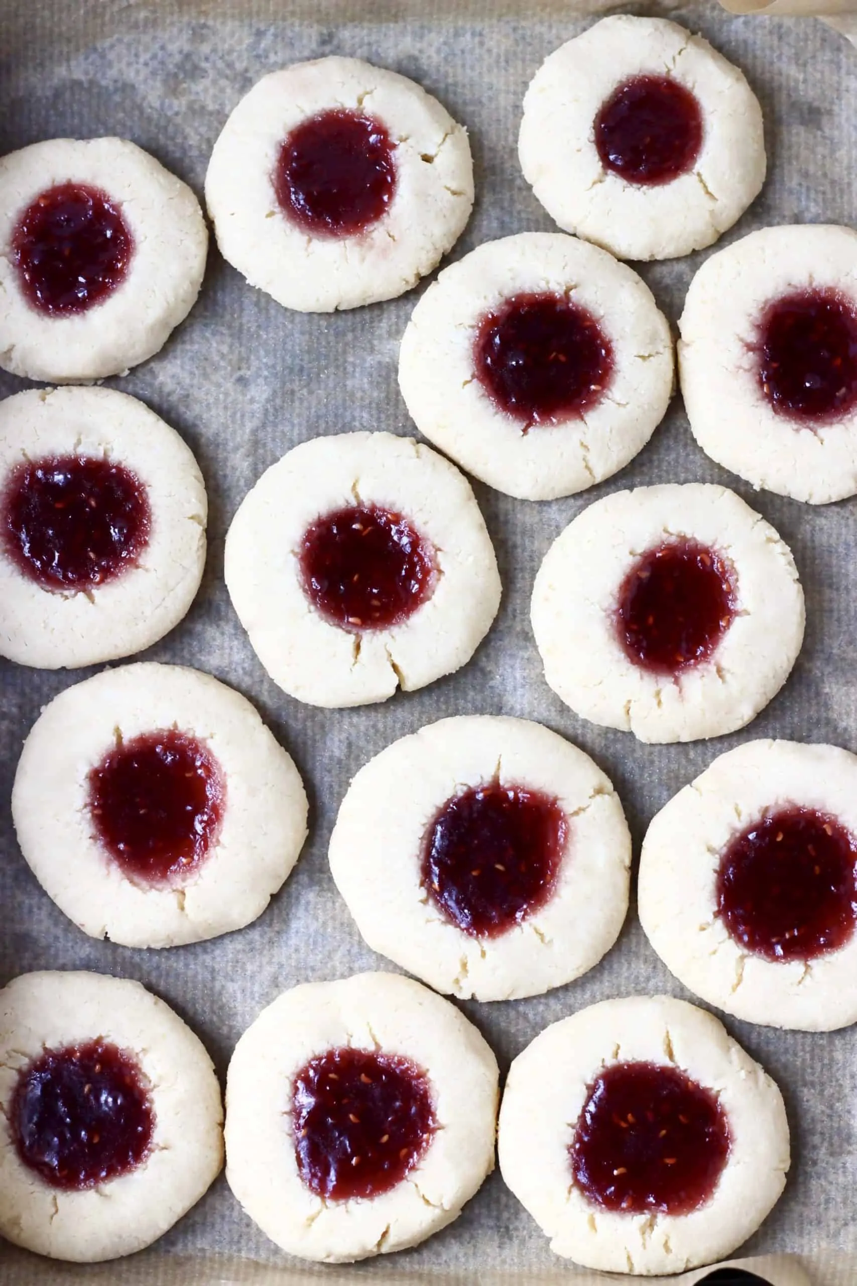 Gluten-free vegan thumbprint cookies filled with raspberry jam on a baking tray lined with baking paper