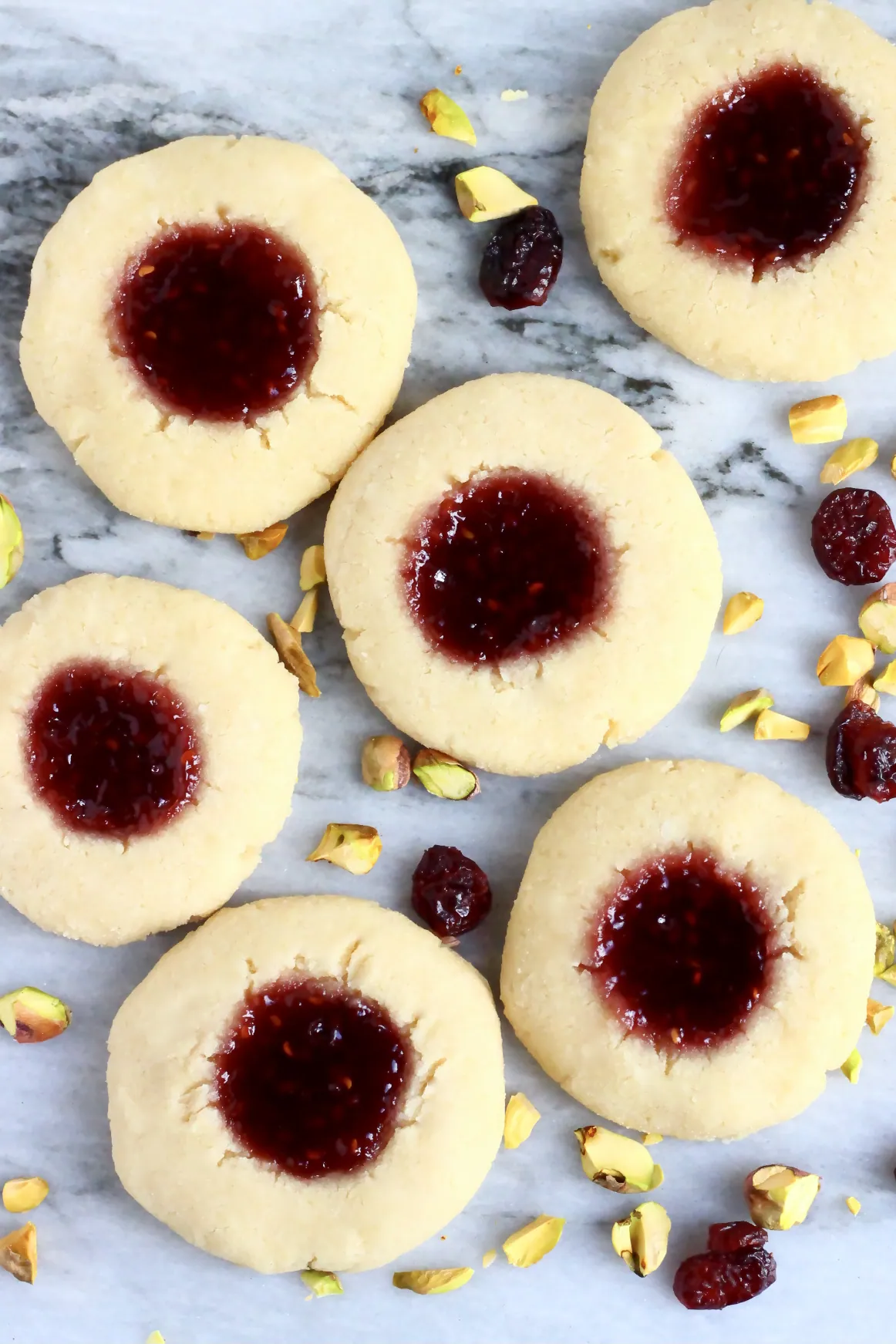Six gluten-free vegan thumbprint cookies with raspberry jam on a marble background