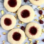 Six gluten-free vegan thumbprint cookies with raspberry jam on a marble background