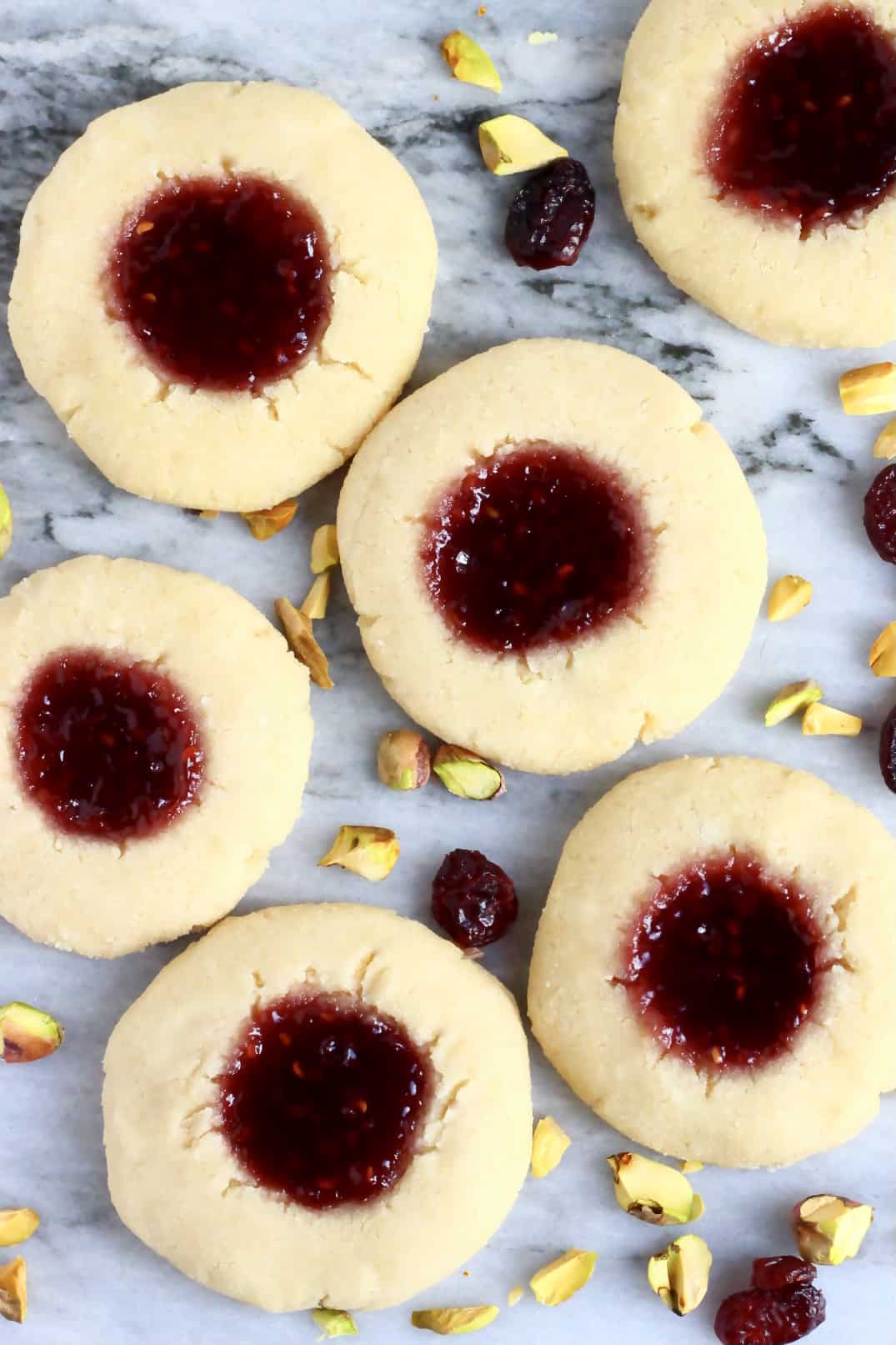Six gluten-free vegan thumbprint cookies with raspberry jam on a marble background
