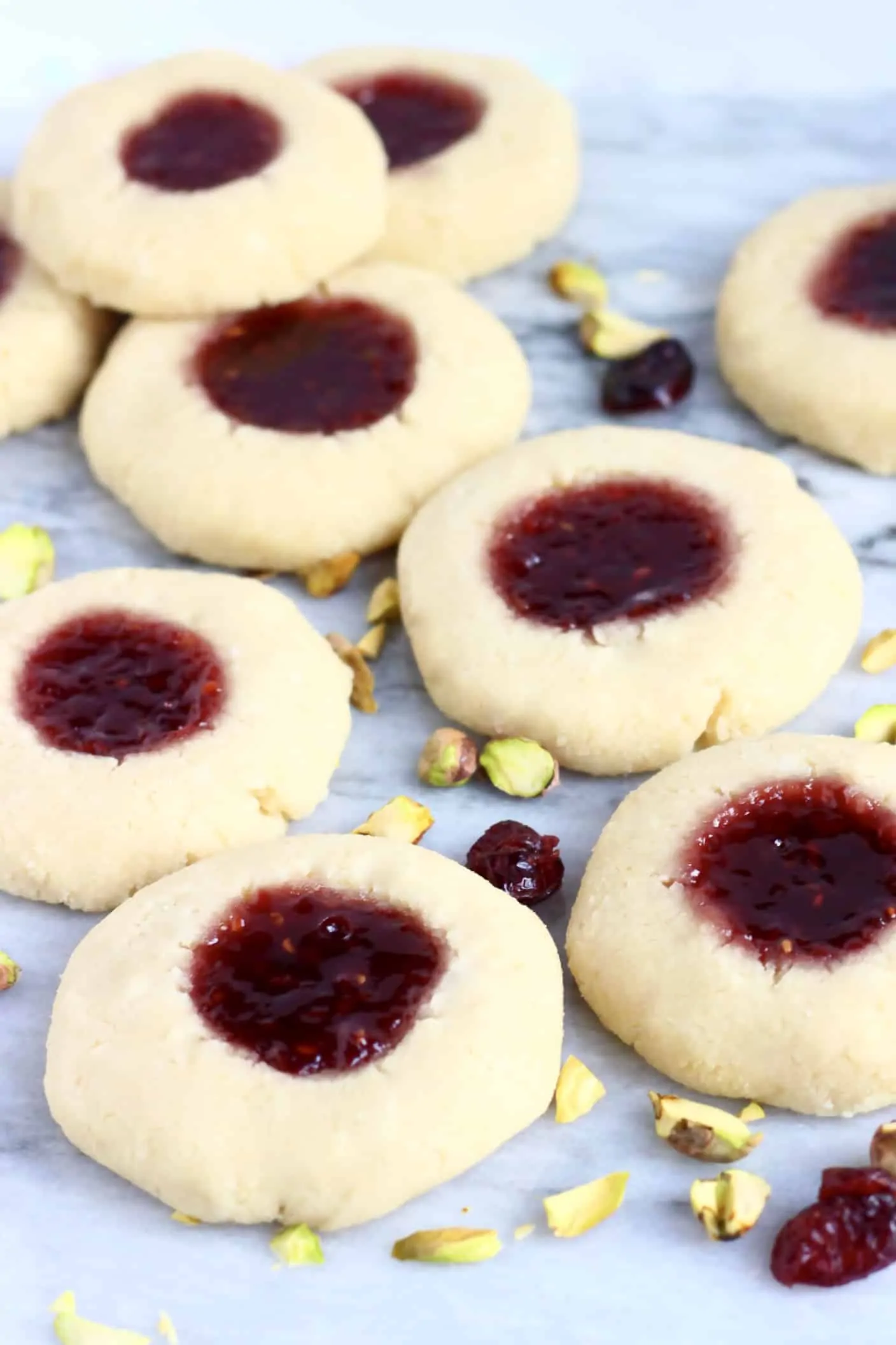 Nine gluten-free vegan thumbprint cookies filled with raspberry jam on a marble background