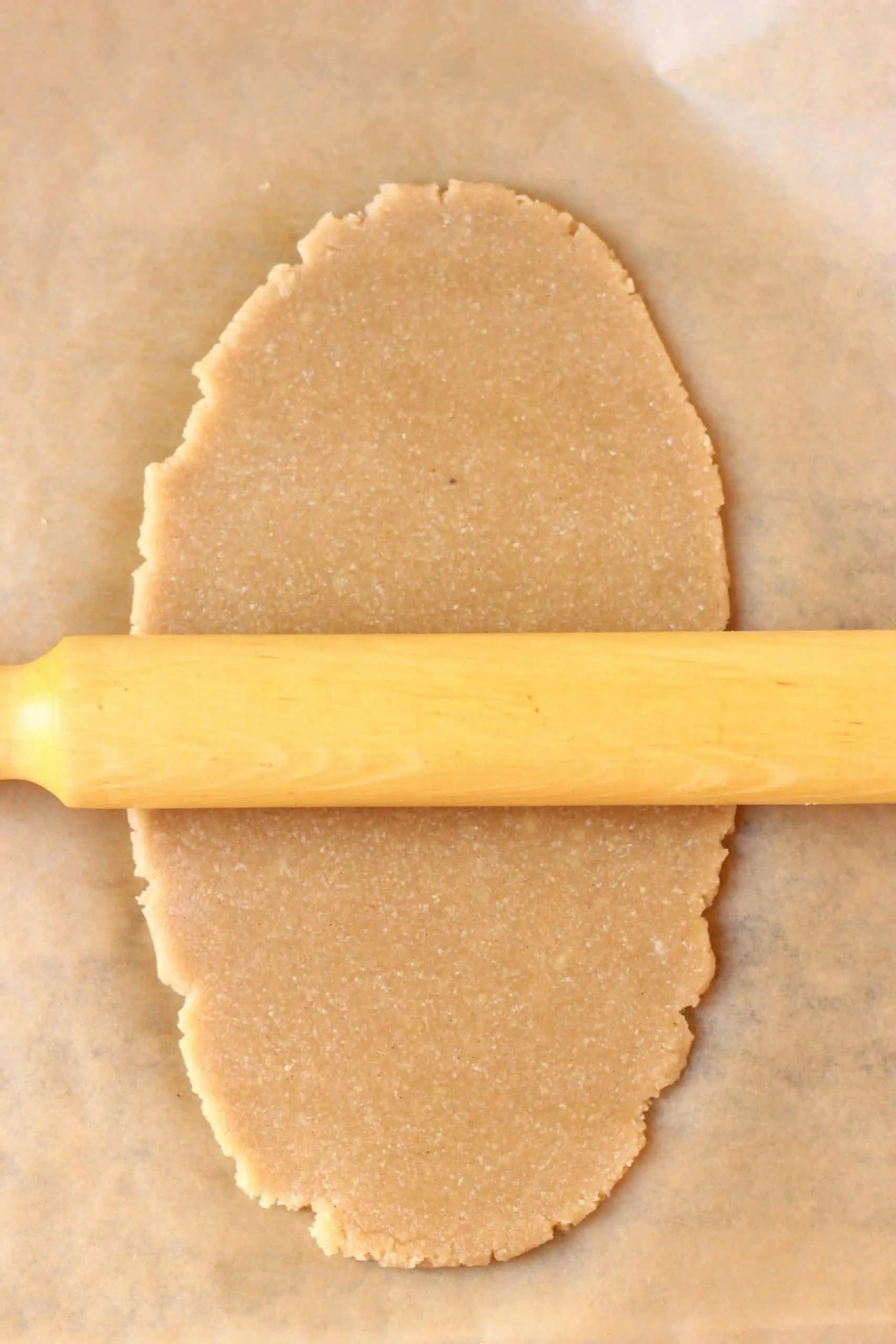 Raw gluten-free vegan linzer cookie dough rolled out with a rolling pin on a sheet of baking paper