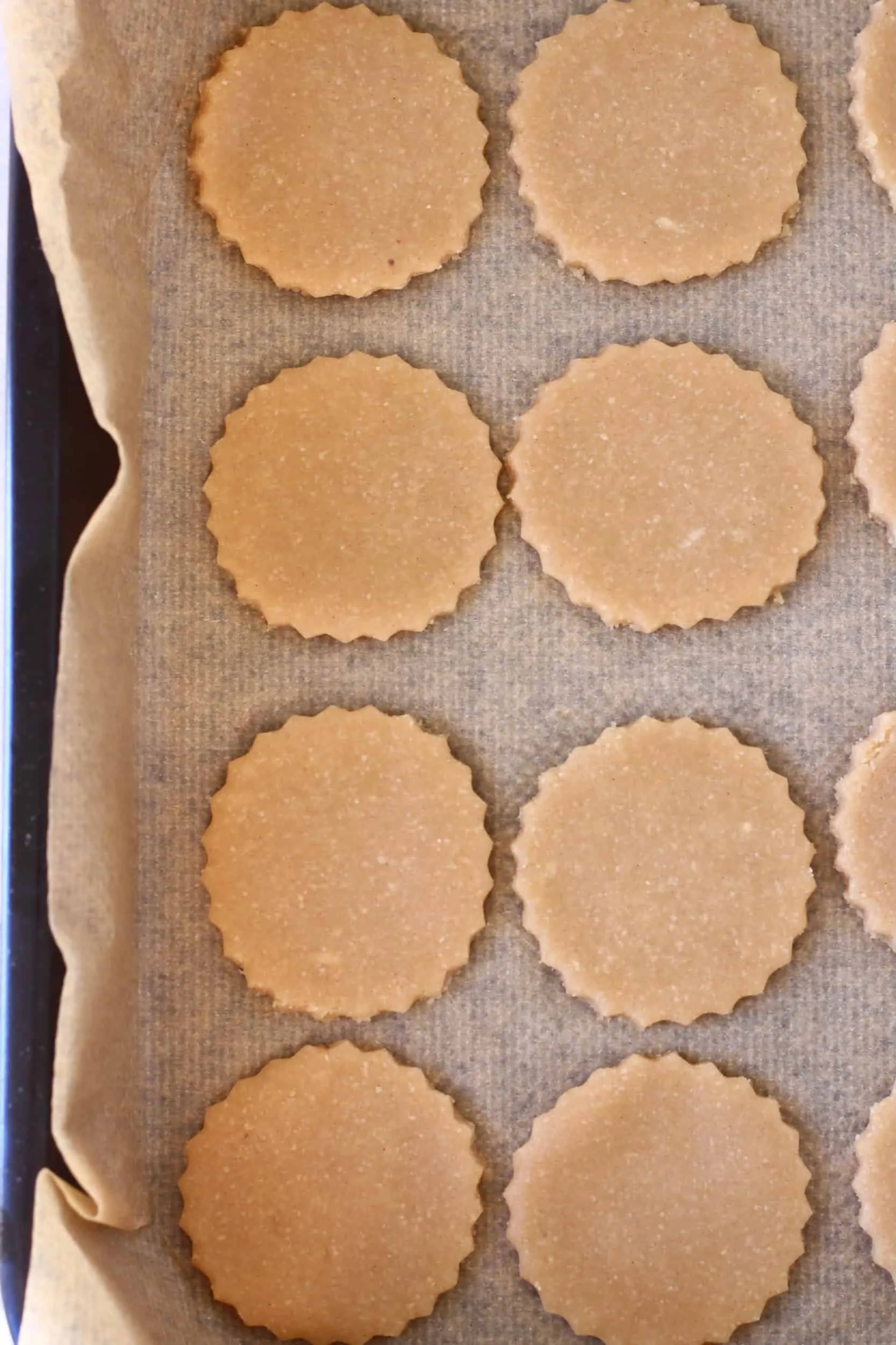 Eight raw gluten-free vegan linzer cookie circles on a baking tray lined with baking paper