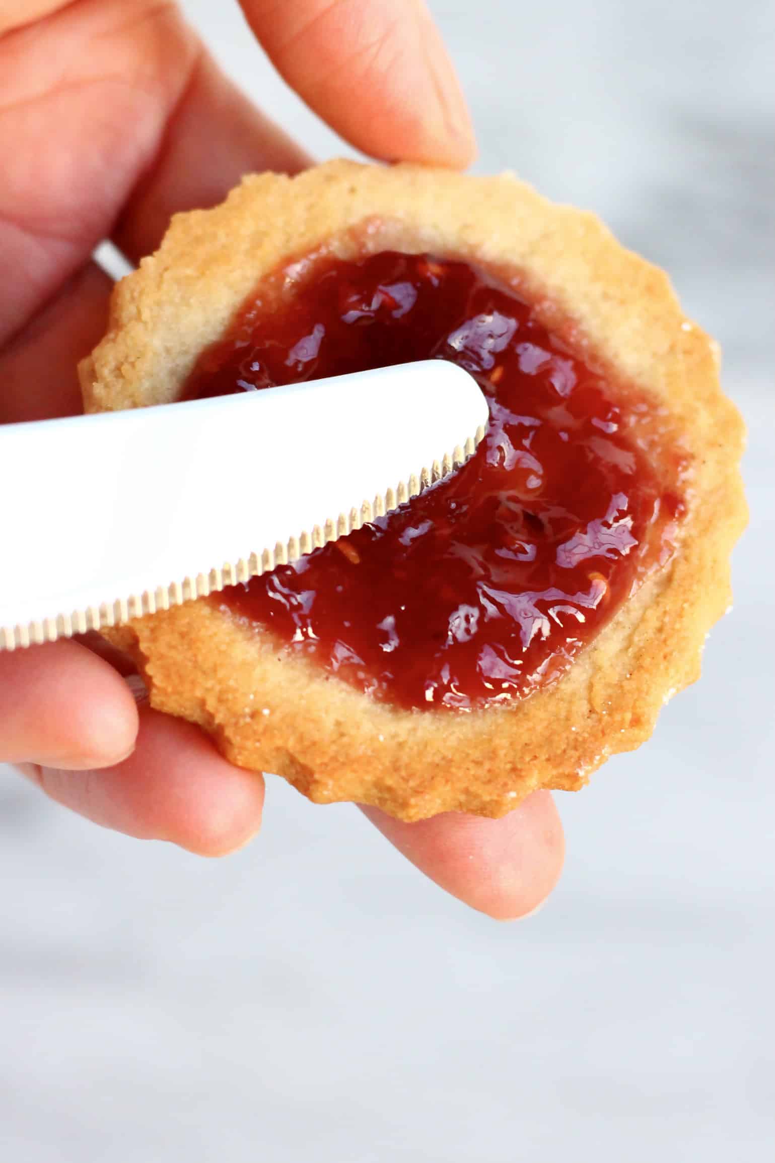 A gluten-free vegan linzer cookie base being spread with raspberry jam