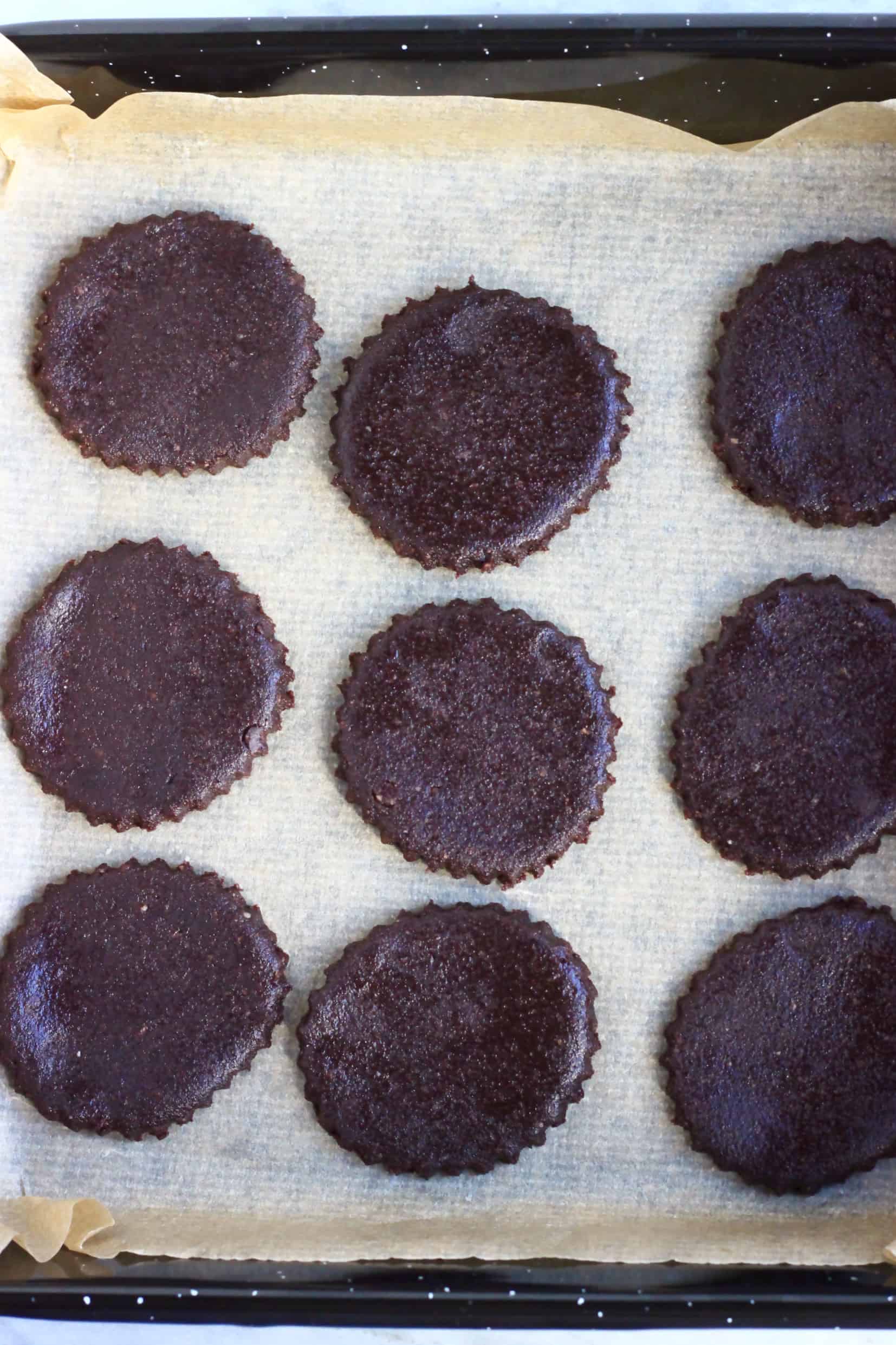 Nine raw gluten-free vegan homemade oreo cookie circles on a baking tray lined with baking paper