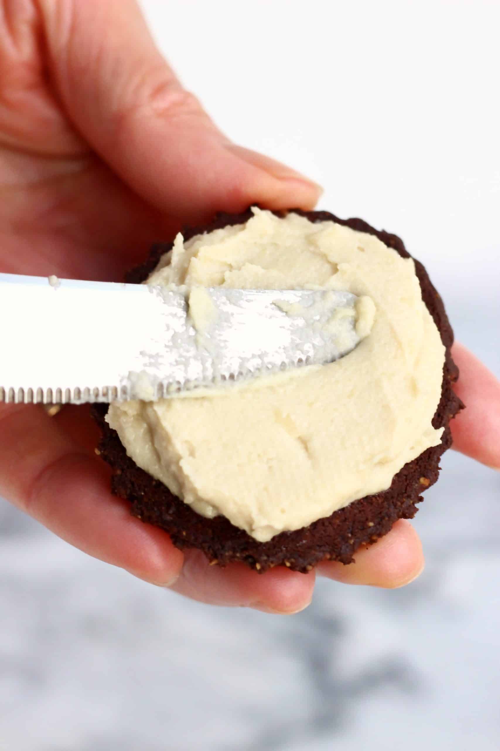 A gluten-free vegan homemade oreo cookie being spread with cream