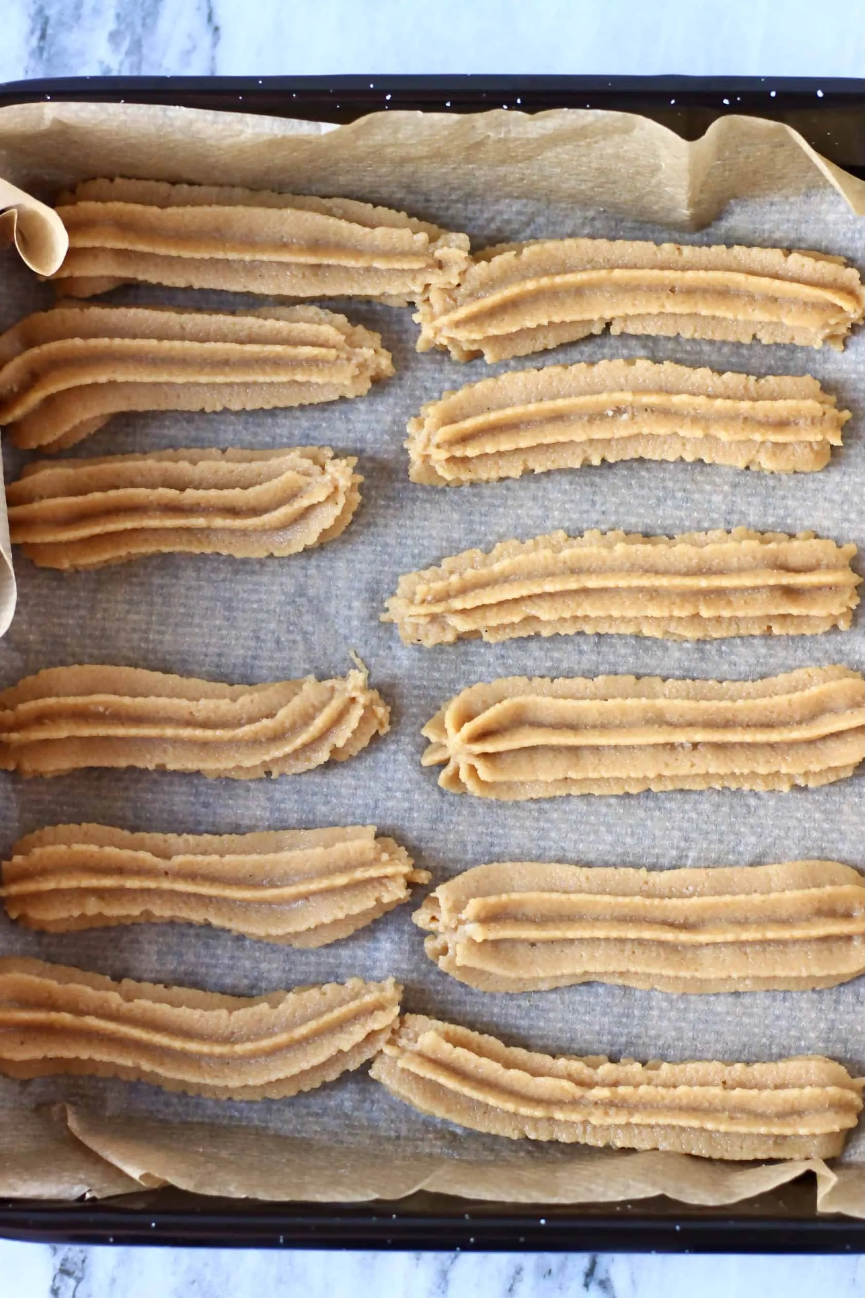 Twelve raw gluten-free vegan churros piped out onto a baking tray lined with baking paper