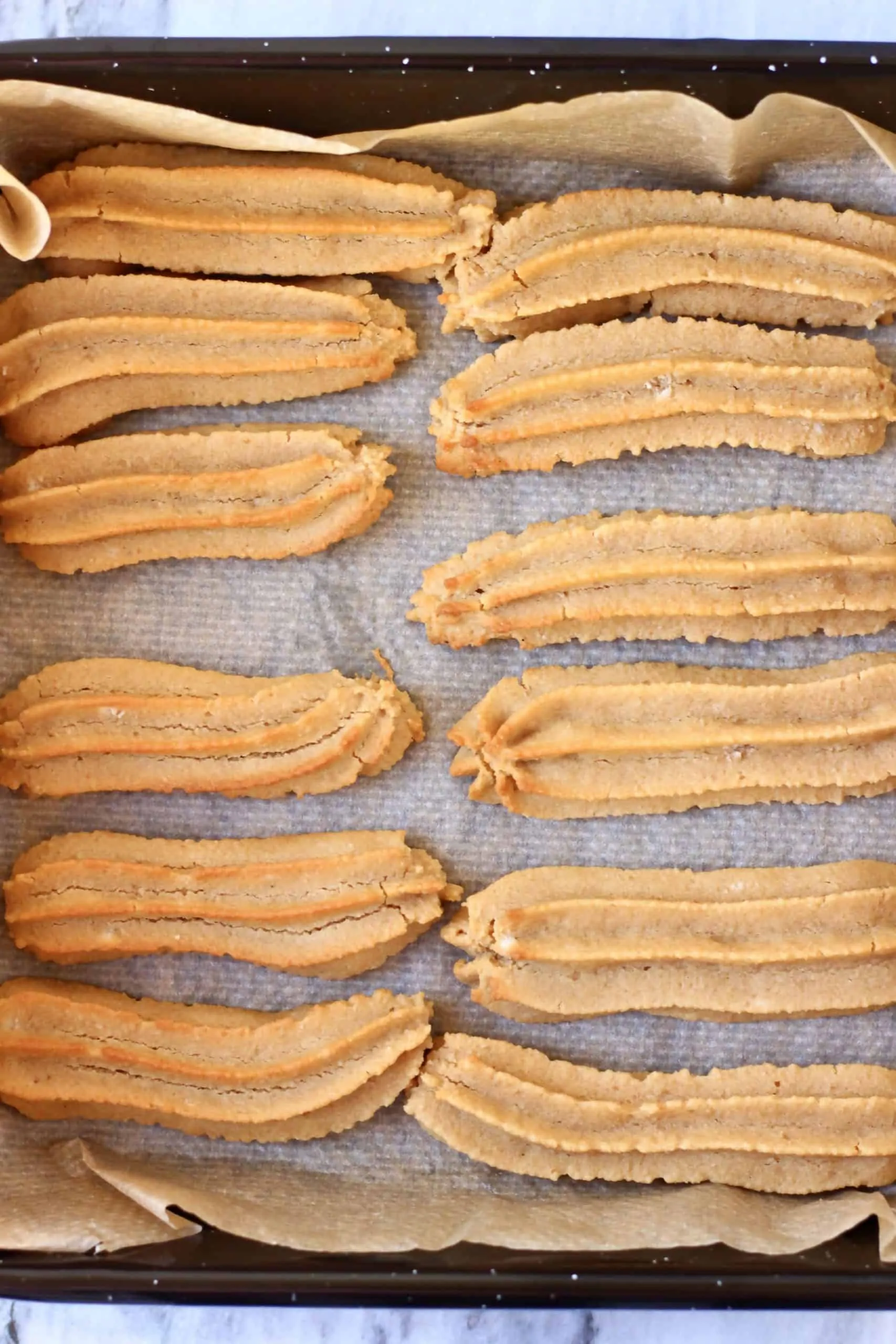 Twelve baked gluten-free vegan churros on a baking tray lined with baking paper