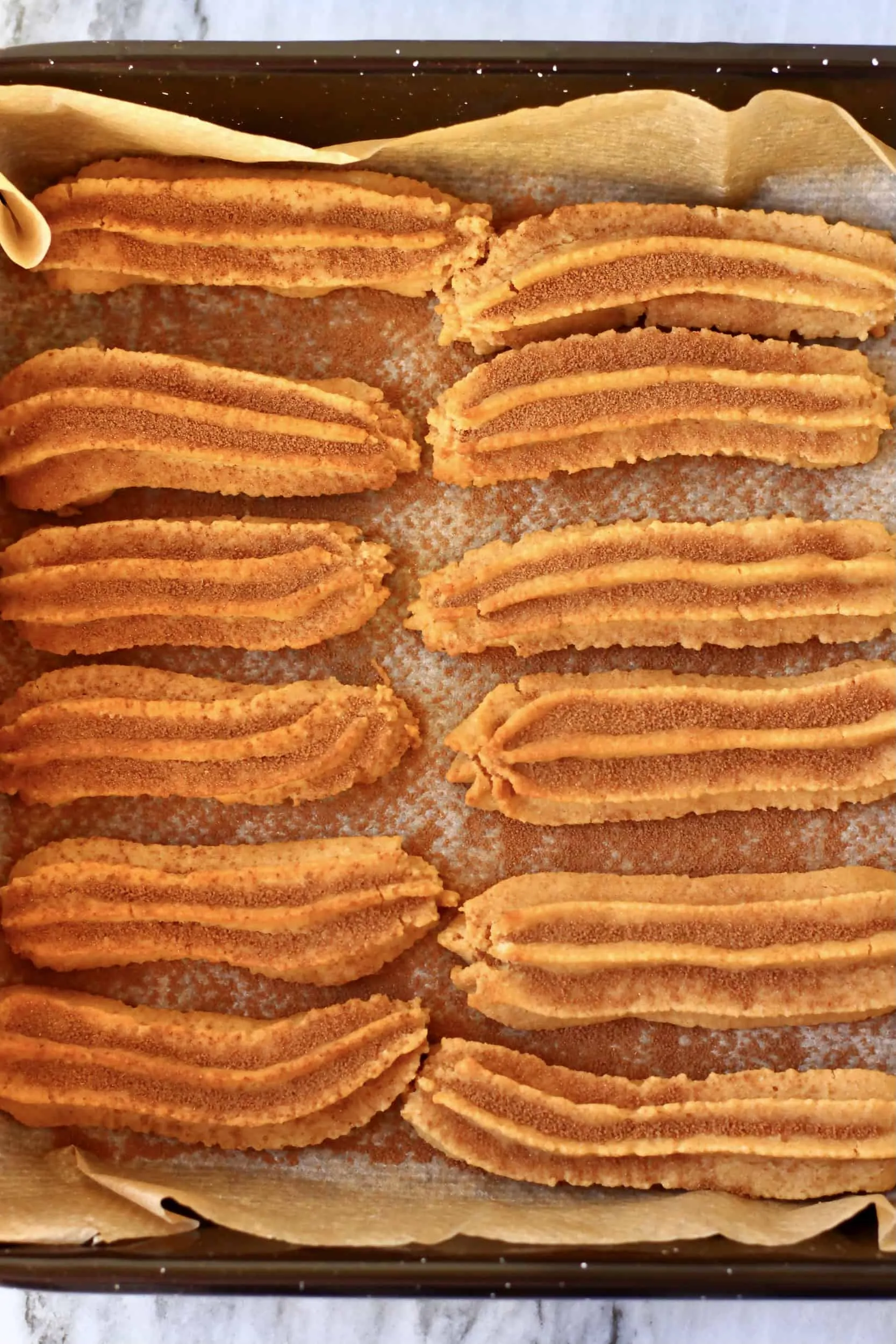 Twelve baked gluten-free vegan churros dusted with cinnamon sugar on a baking tray