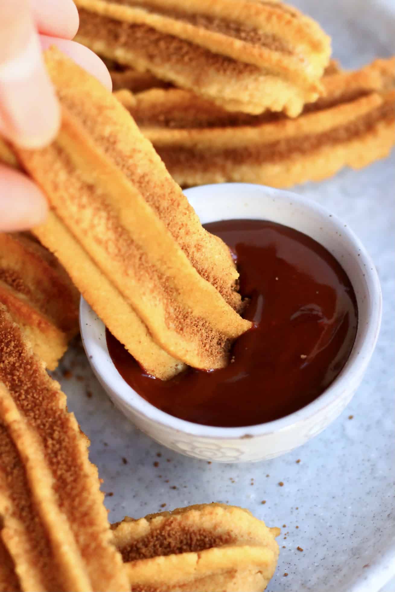 A gluten-free vegan churro being dipped into a bowl of vegan chocolate sauce