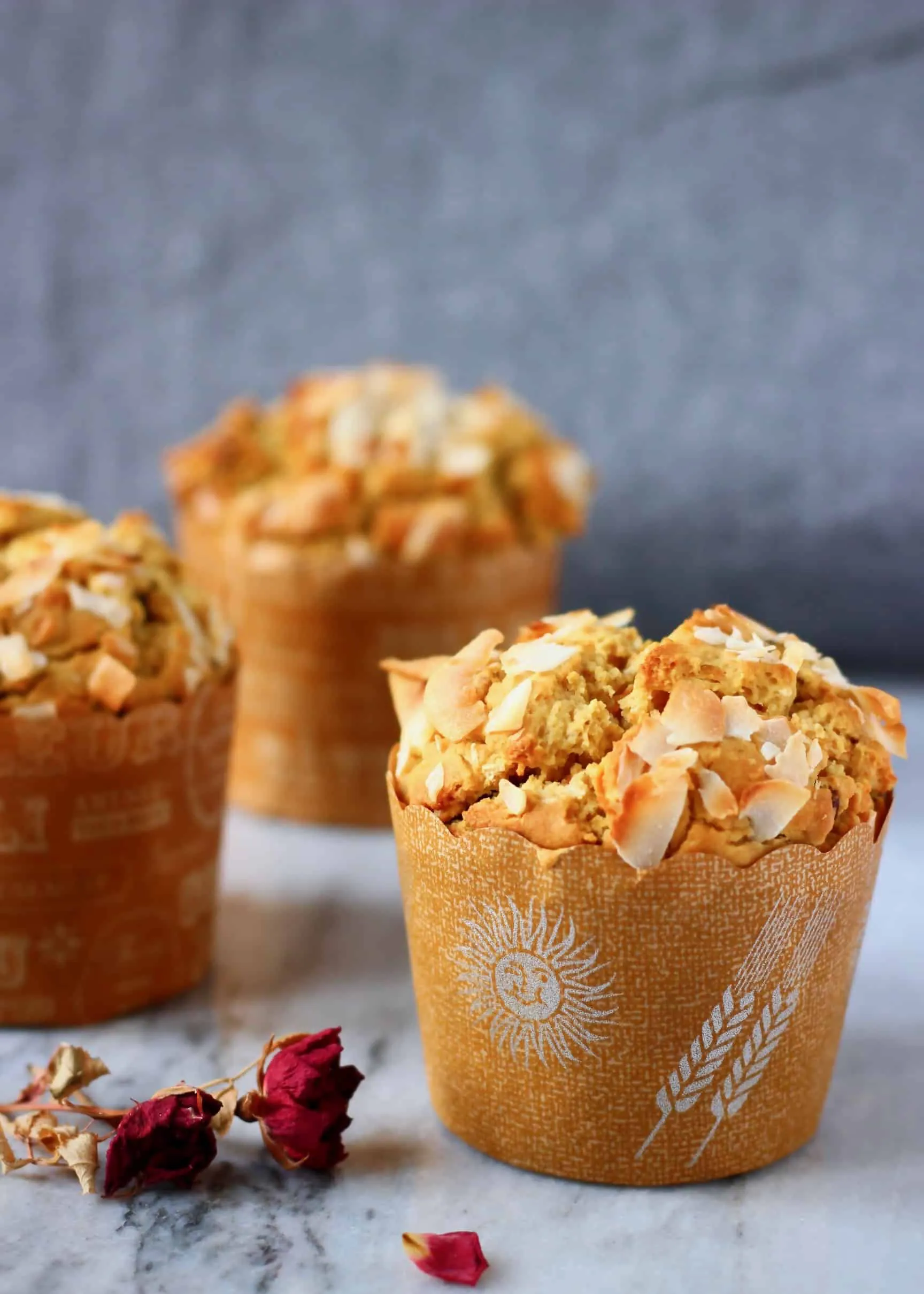 Three gluten-free vegan carrot muffins on a marble slab with a grey fabric background