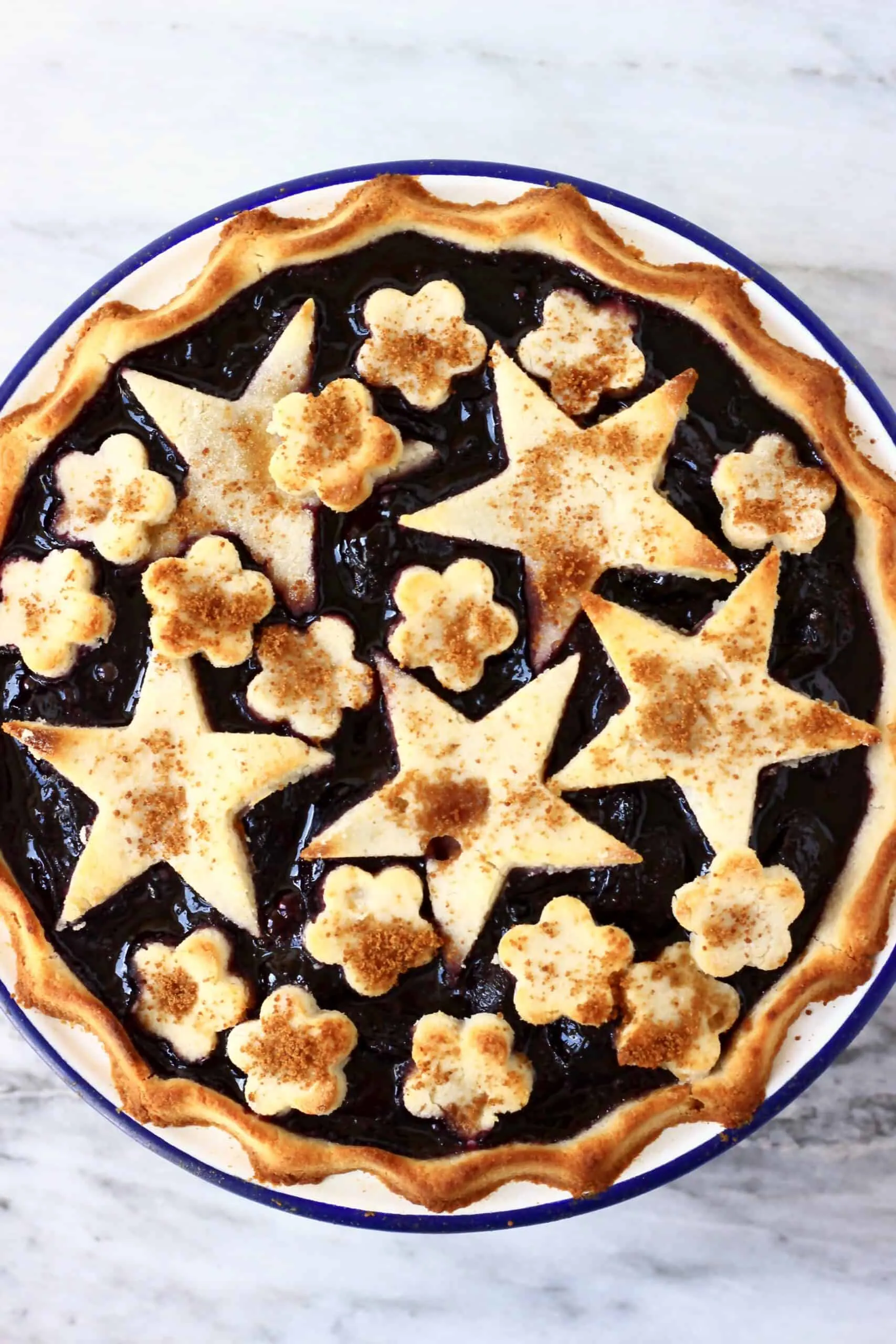 Gluten-free vegan cherry pie topped with stars and flowers in a white pie dish with a blue rim against a marble background