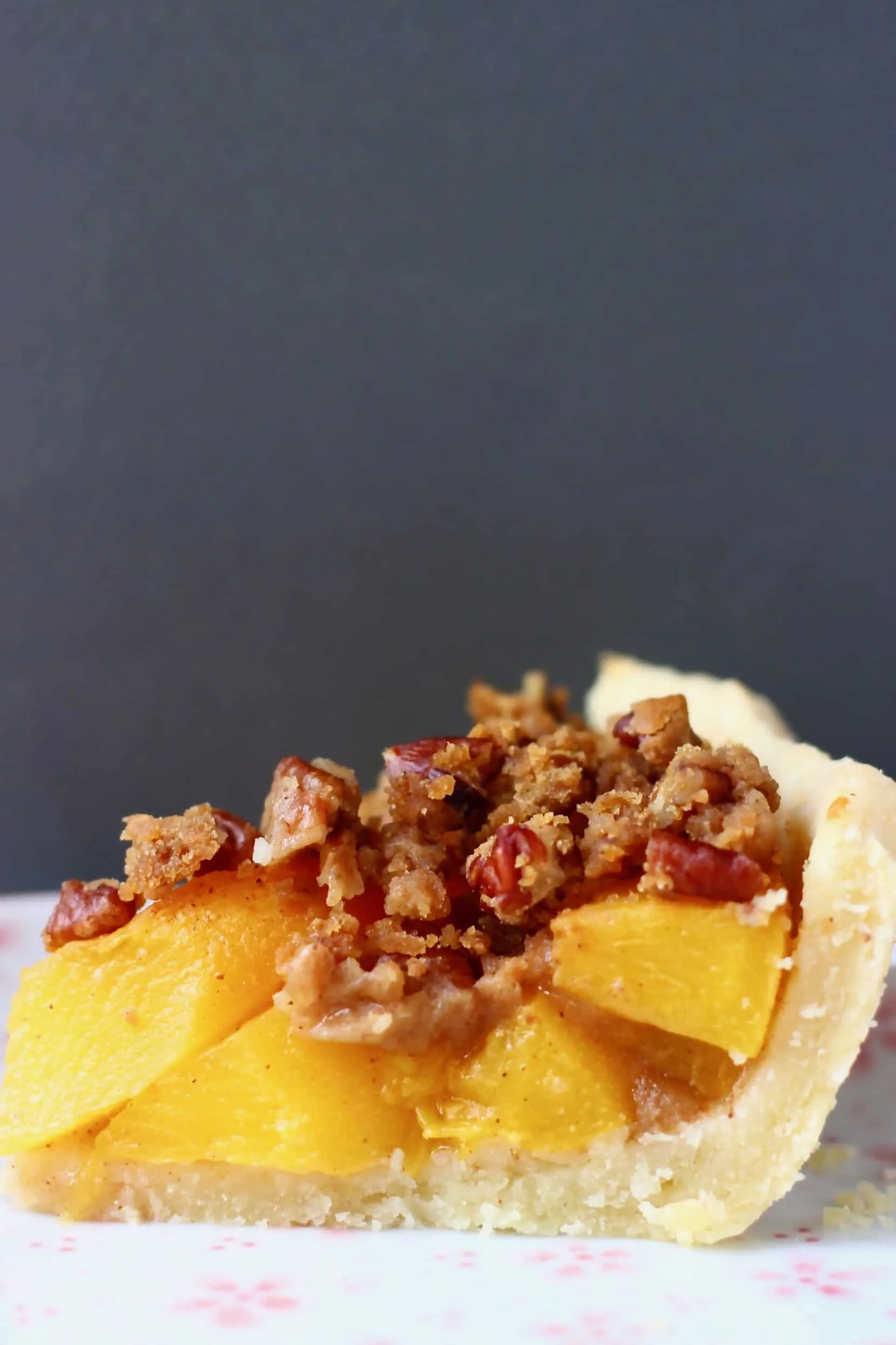 A slice of gluten-free vegan peach pie on a white plate with a gold fork and a grey background