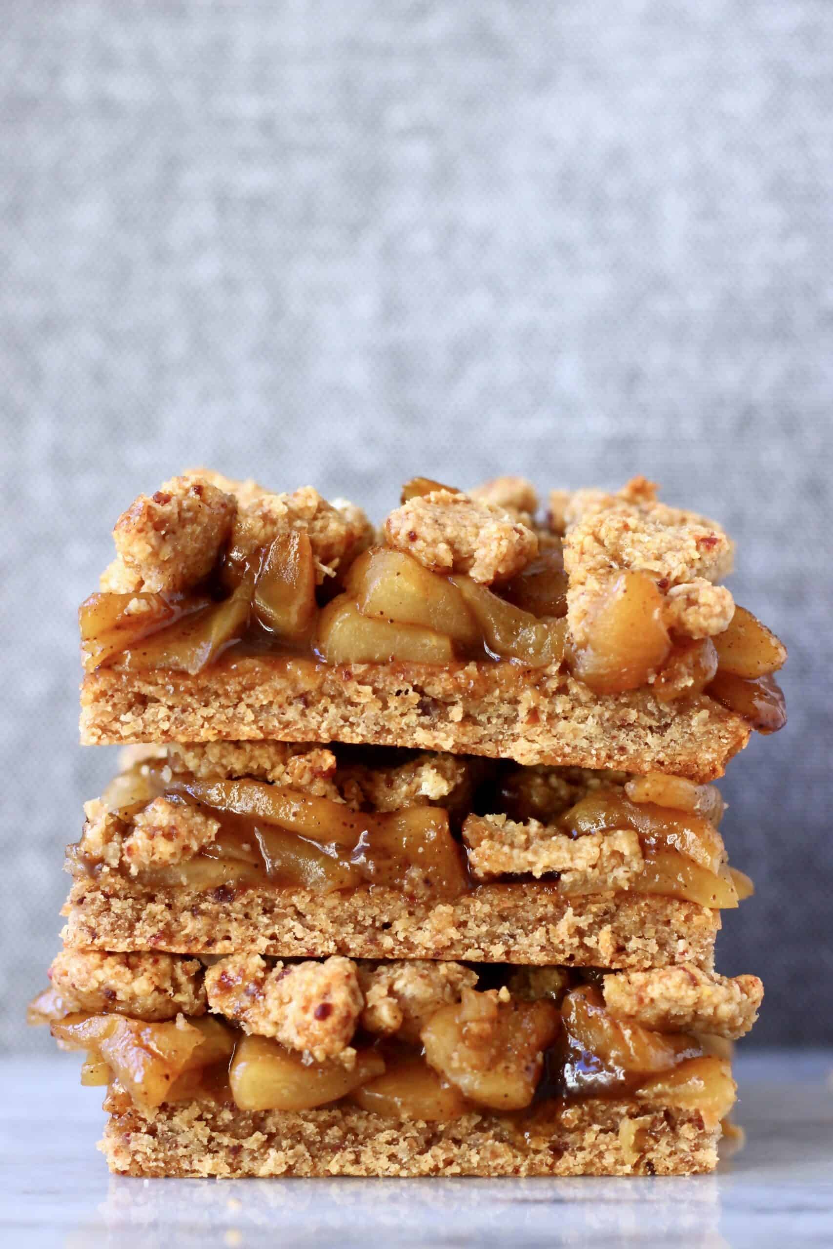 A stack of three gluten-free vegan apple crumble bars on a marble slab against a grey background