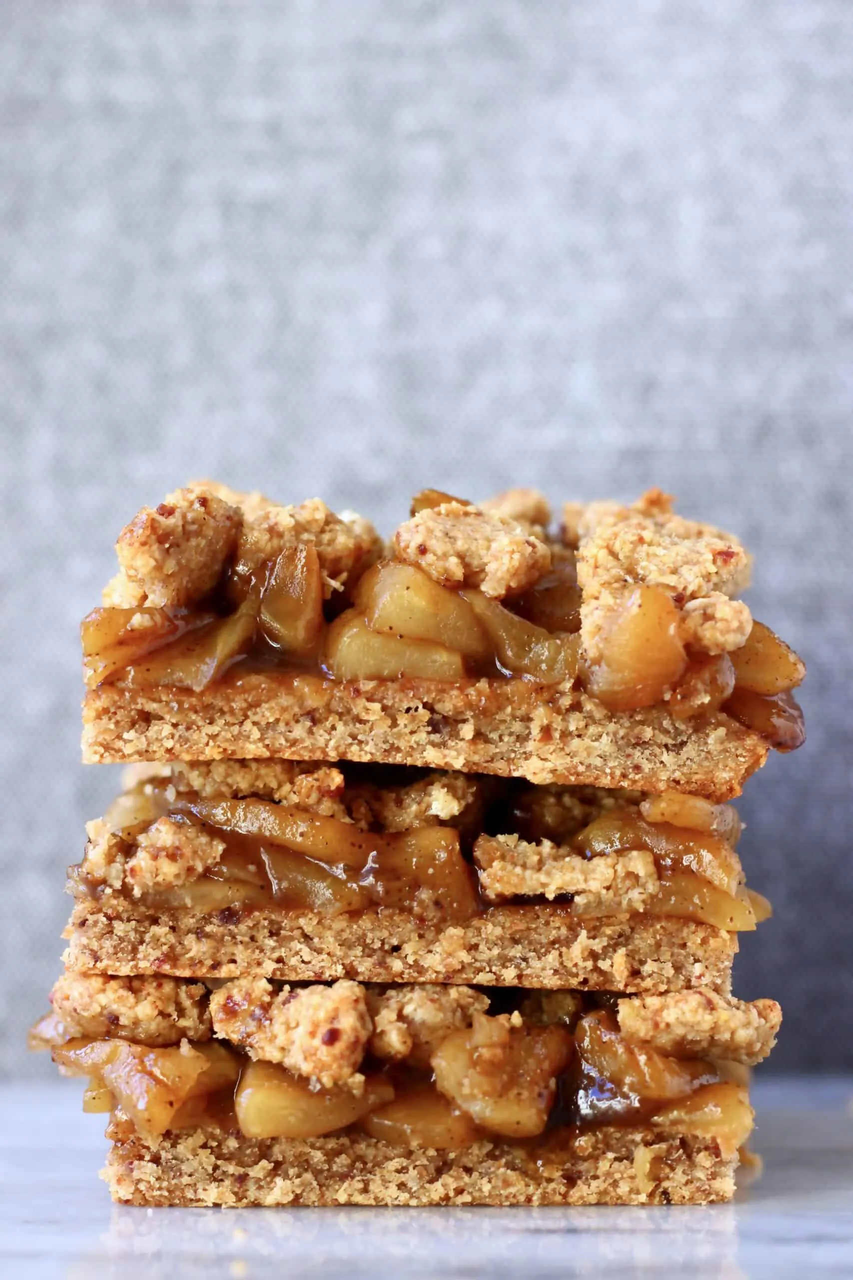 A stack of three gluten-free vegan apple crumble bars on a marble slab against a grey background