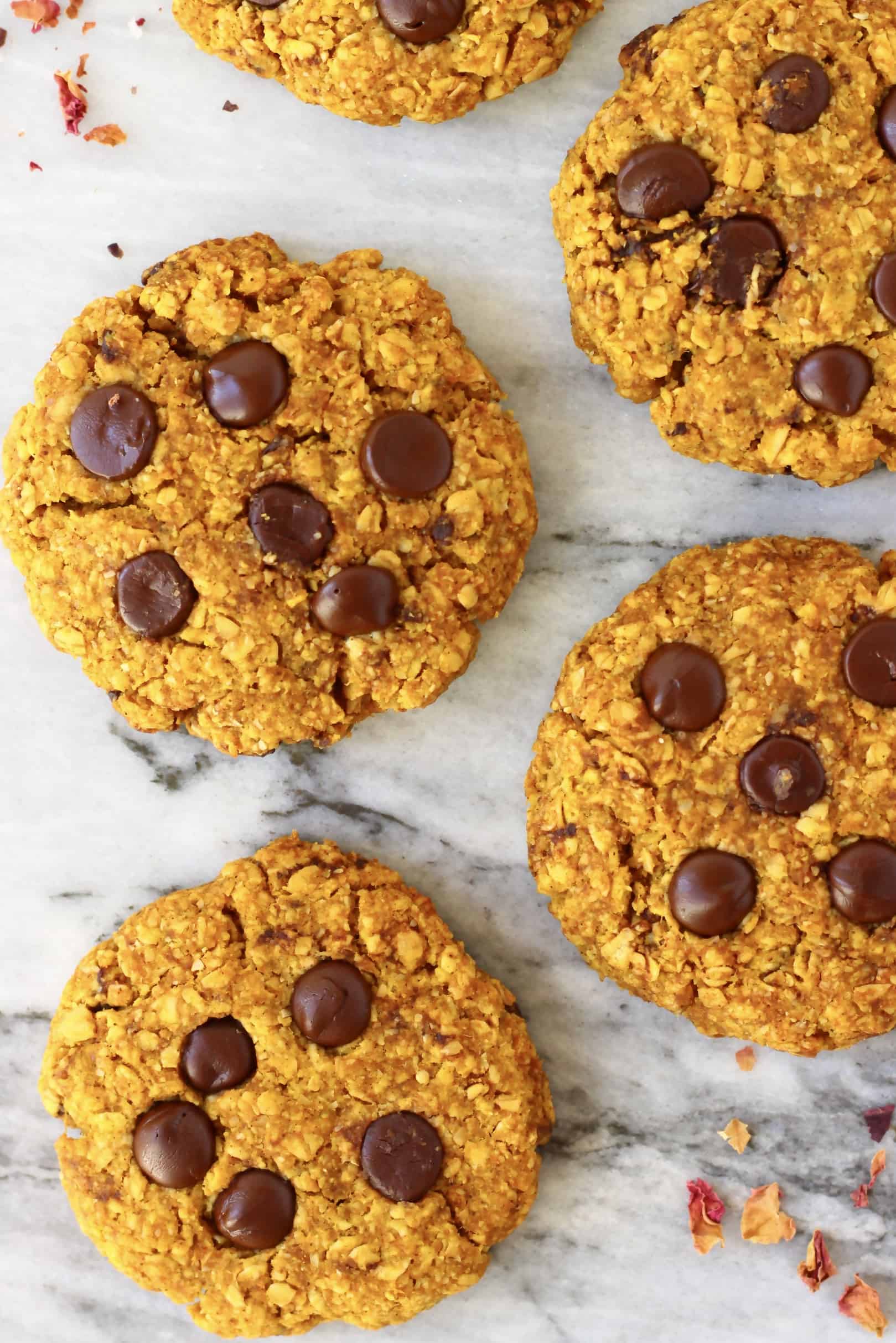 Five gluten-free vegan pumpkin cookies with chocolate chips against a marble background