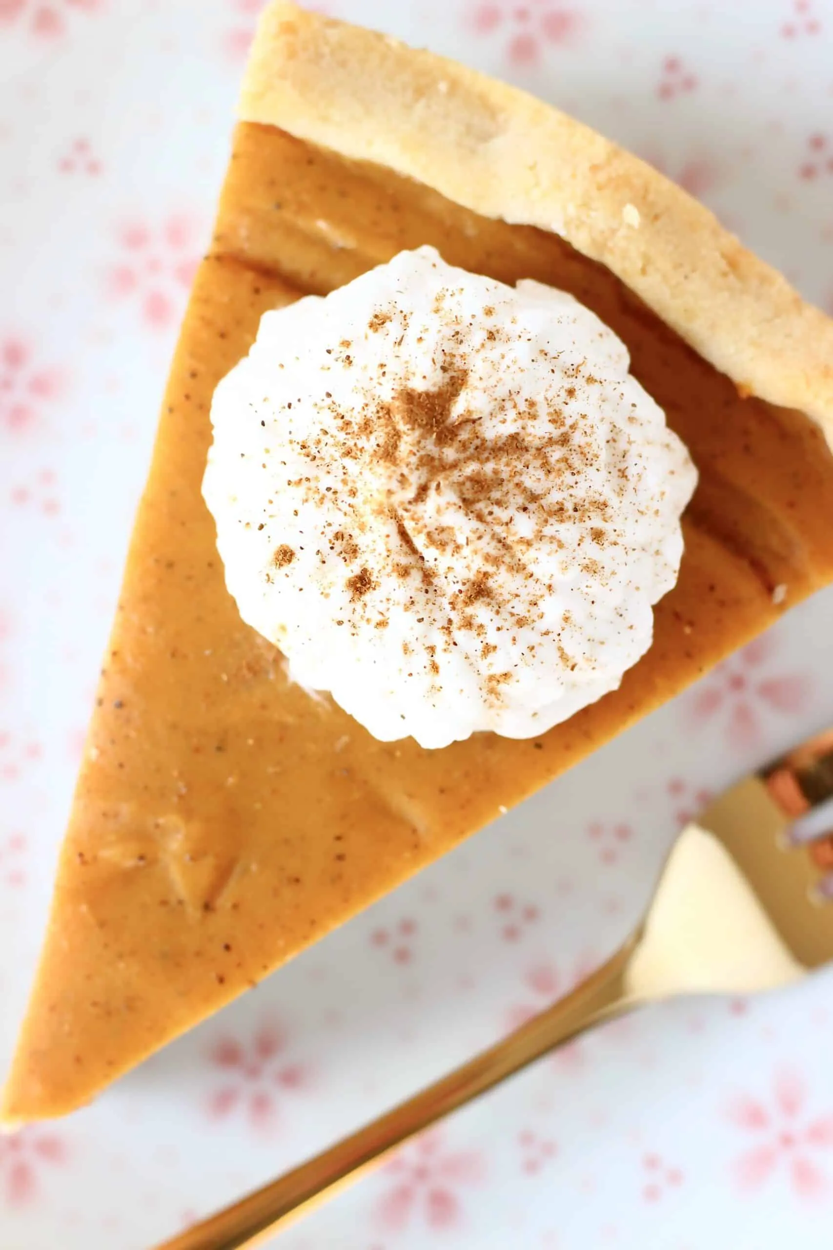 A slice of gluten-free vegan sweet potato pie topped with white cream on a plate with a gold fork