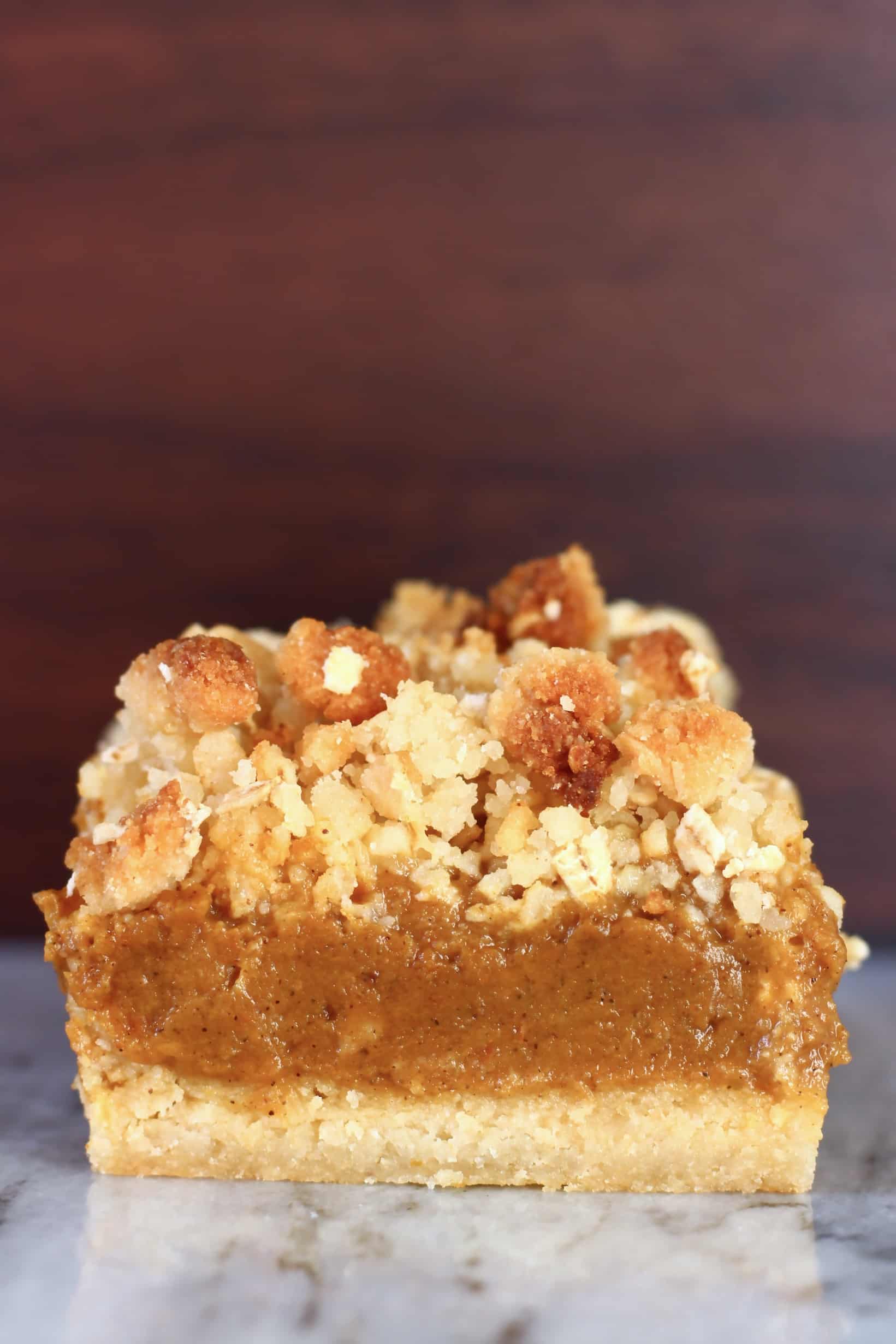 A vegan pumpkin pie bar with crumble topping against a brown background