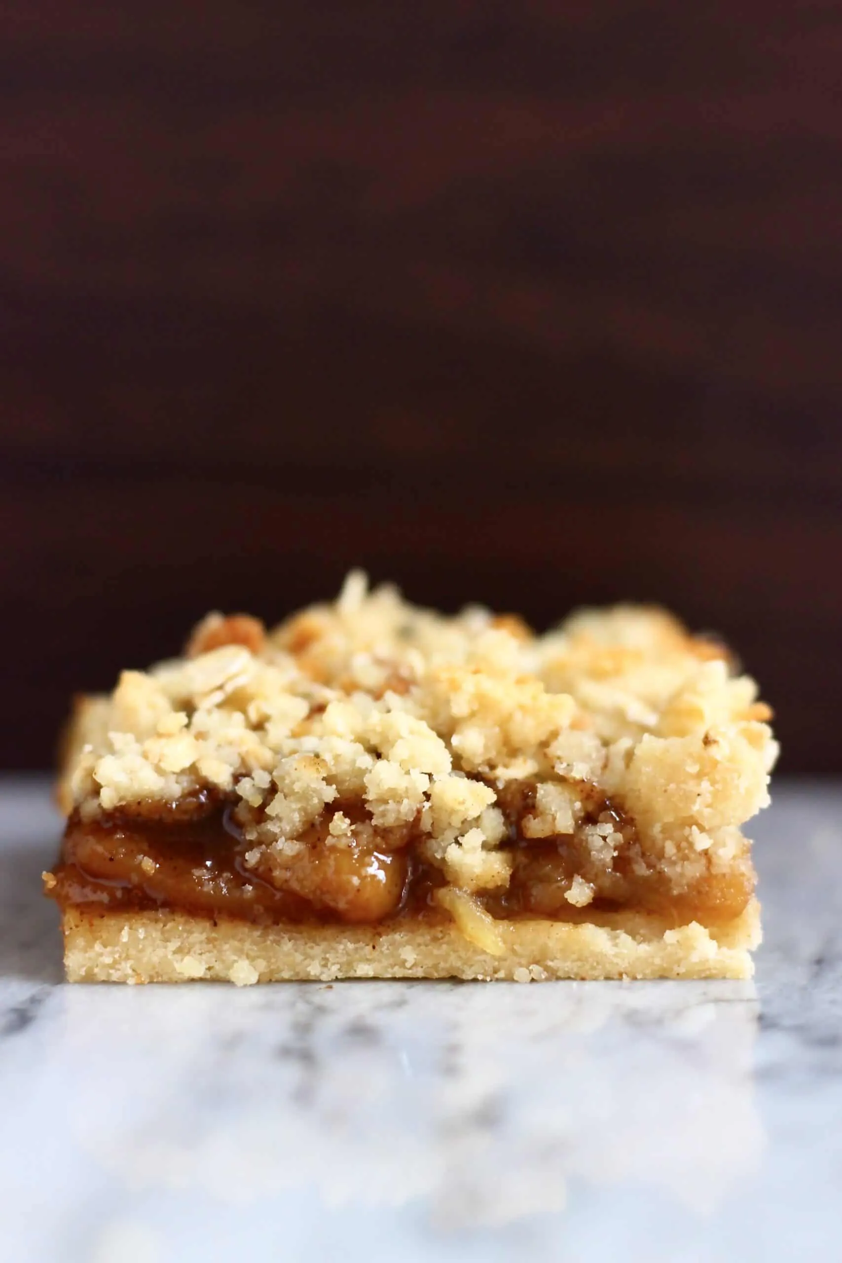 Gluten-free vegan apple pie bar on a marble slab against a dark brown background