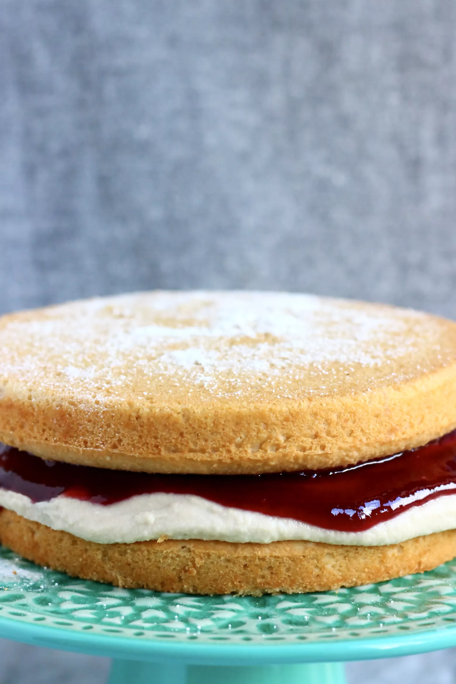 A gluten-free vegan Victoria sponge cake with buttercream and jam on a cake stand