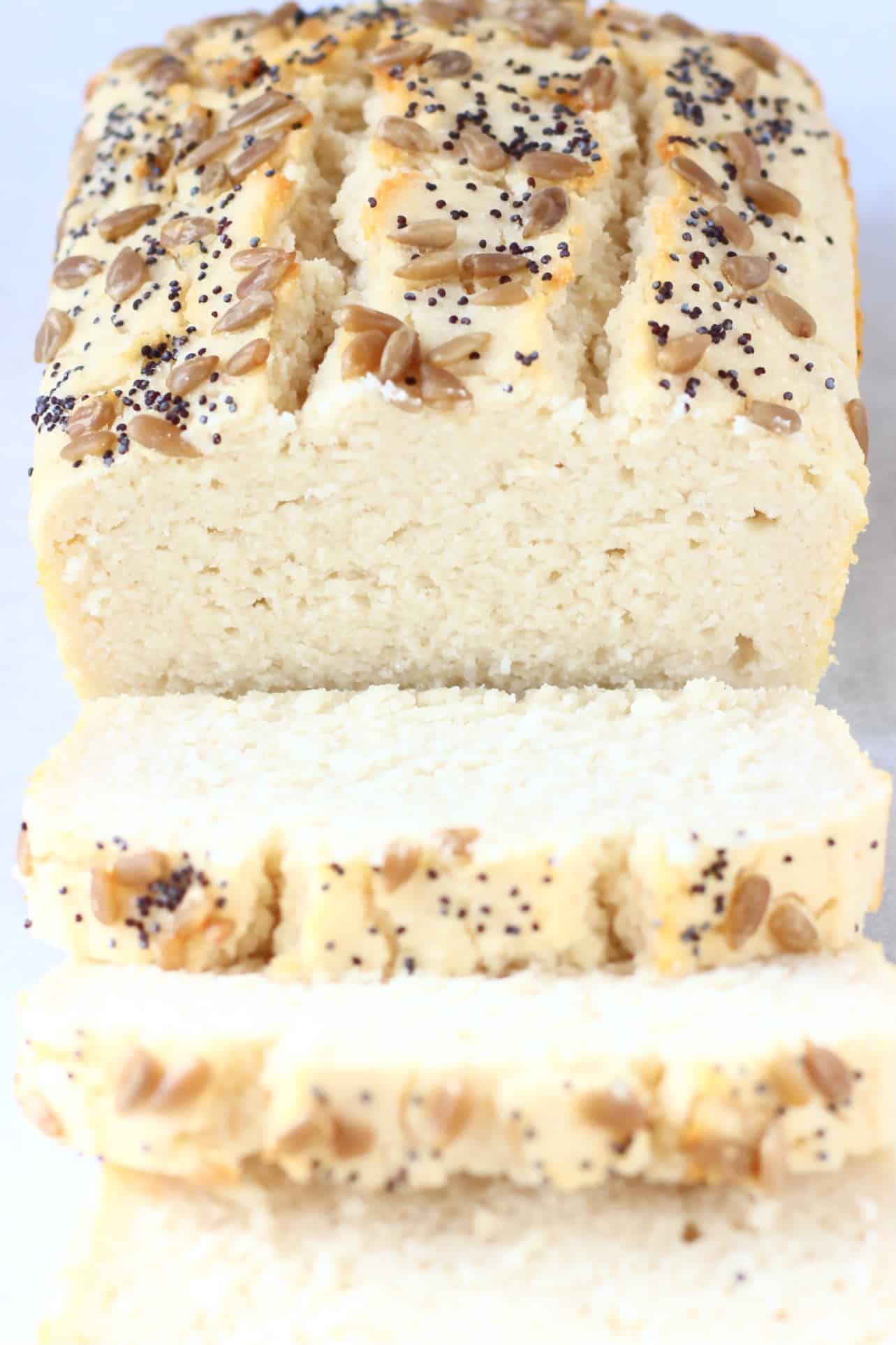 A loaf of coconut flour bread topped with sunflower seeds and poppy seeds with three slices next to it