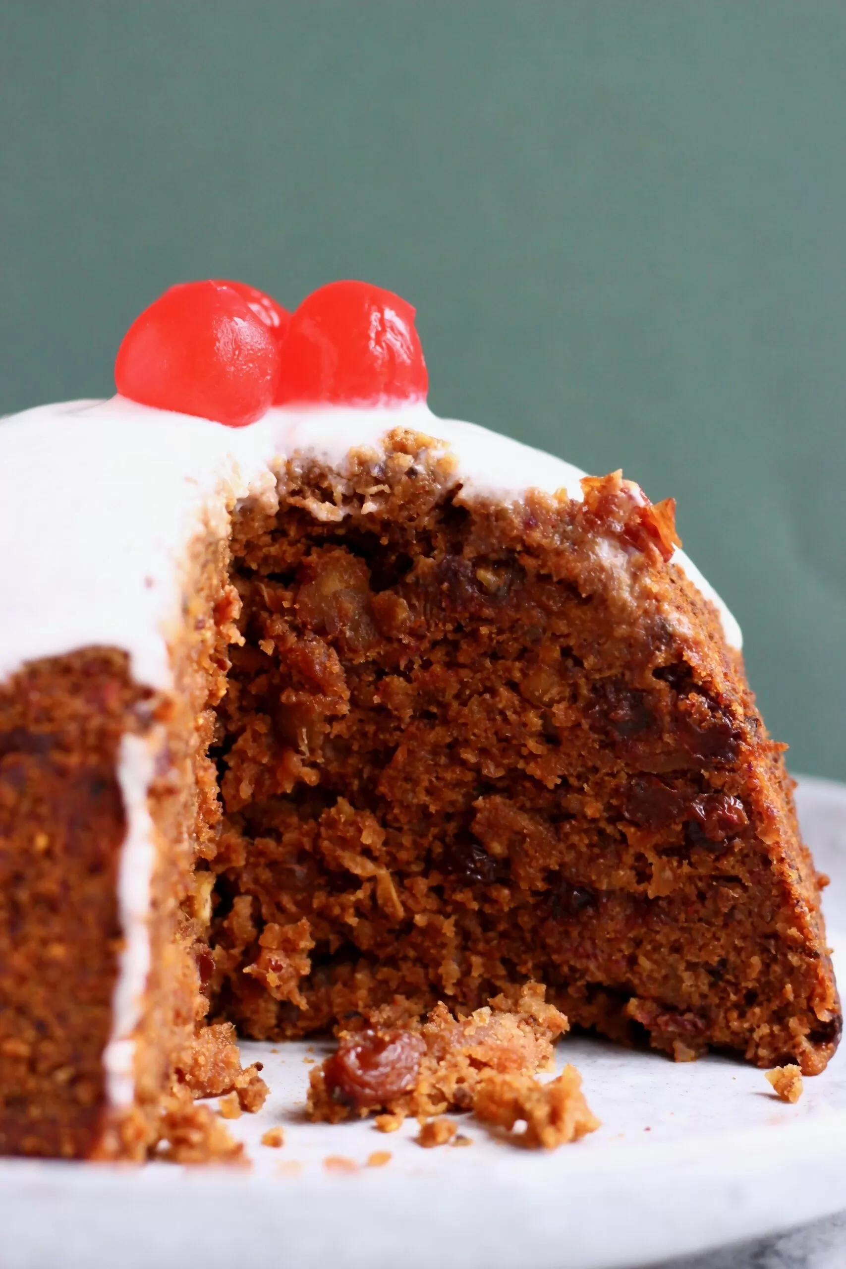 A round gluten-free vegan Christmas pudding with white cream poured over it topped with three red cherries