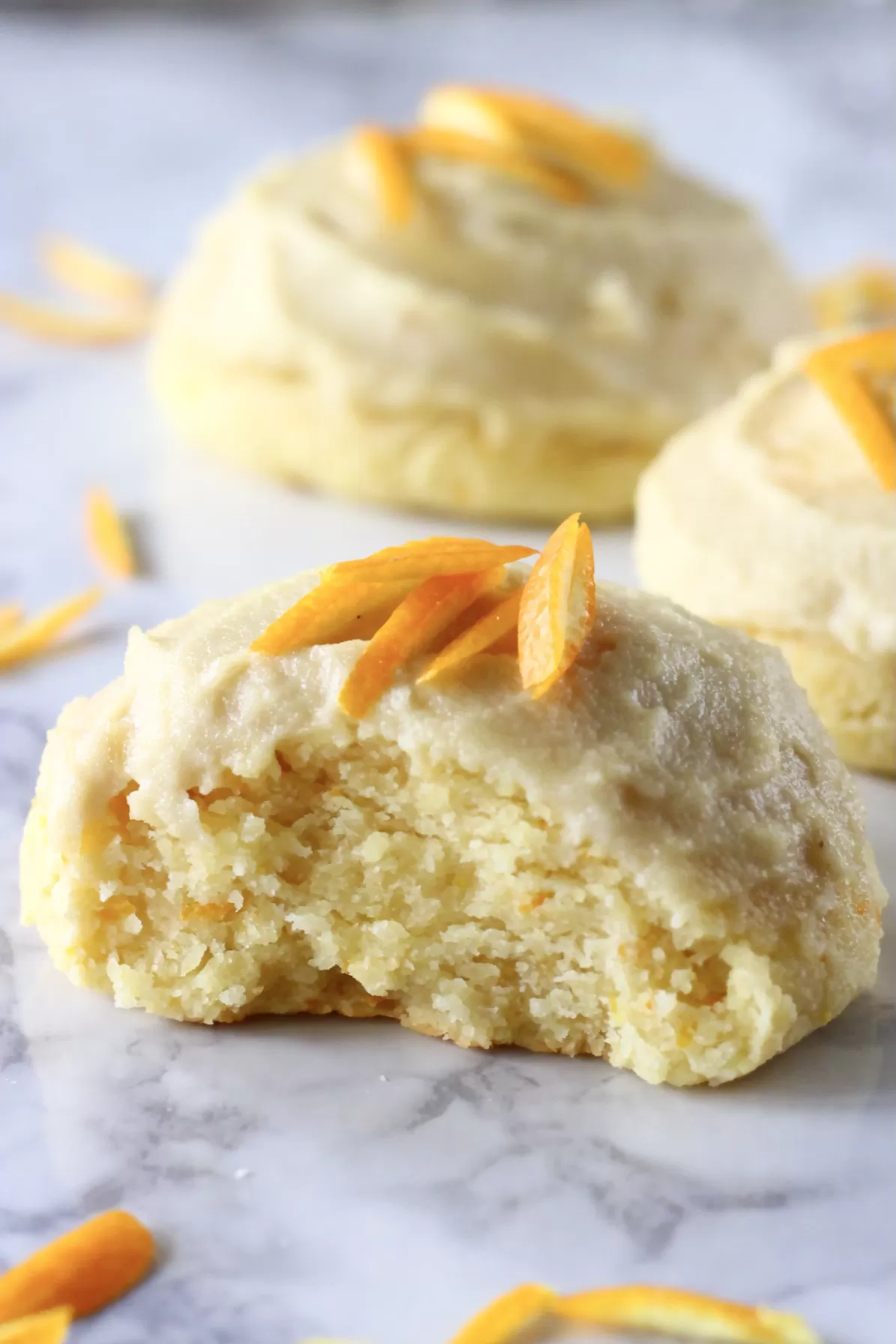 Three gluten-free vegan orange cookies with frosting and orange zest with a bite taken out of one