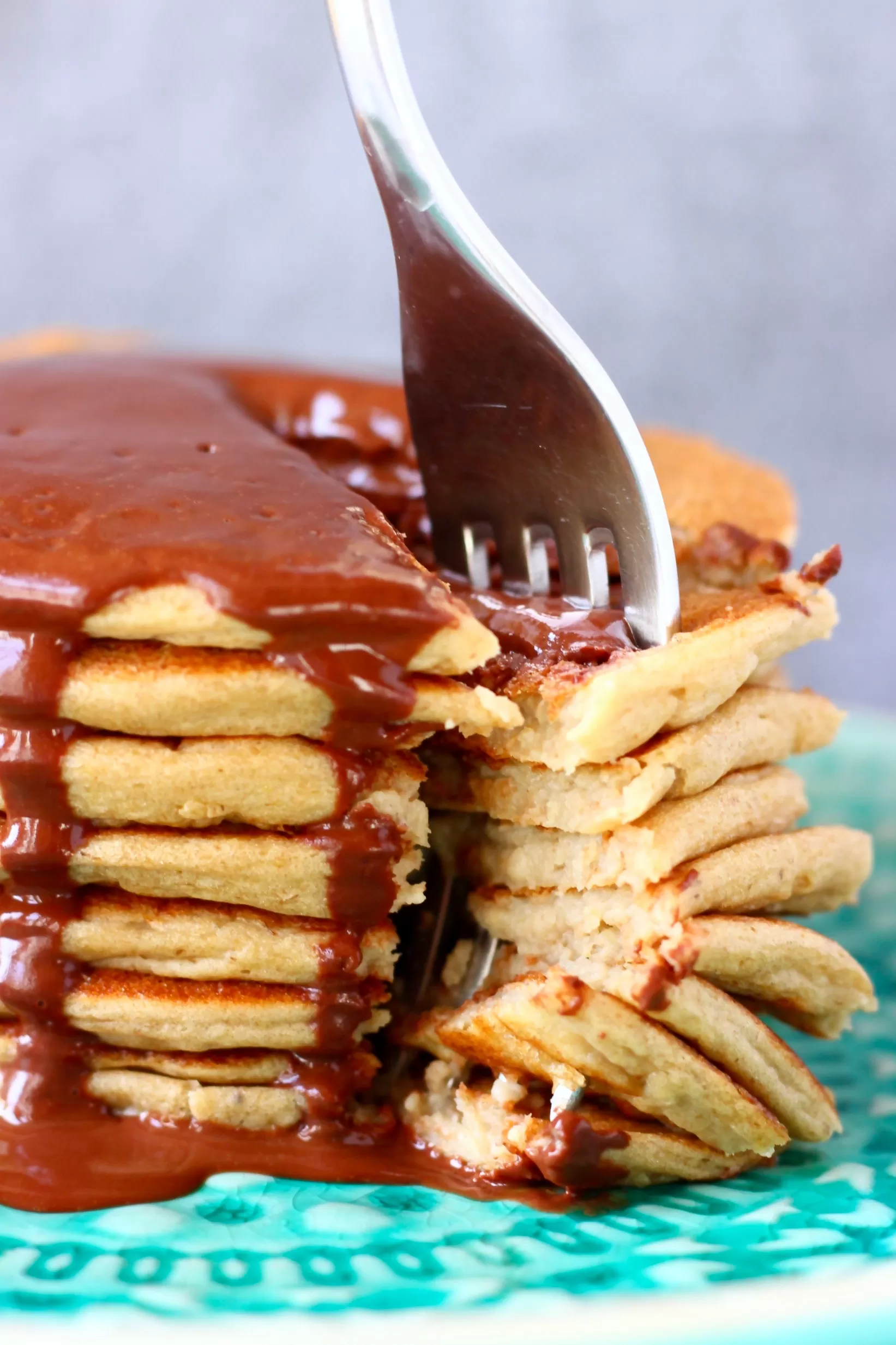 A stack of gluten-free vegan protein pancakes covered in chocolate sauce with a fork sticking into it