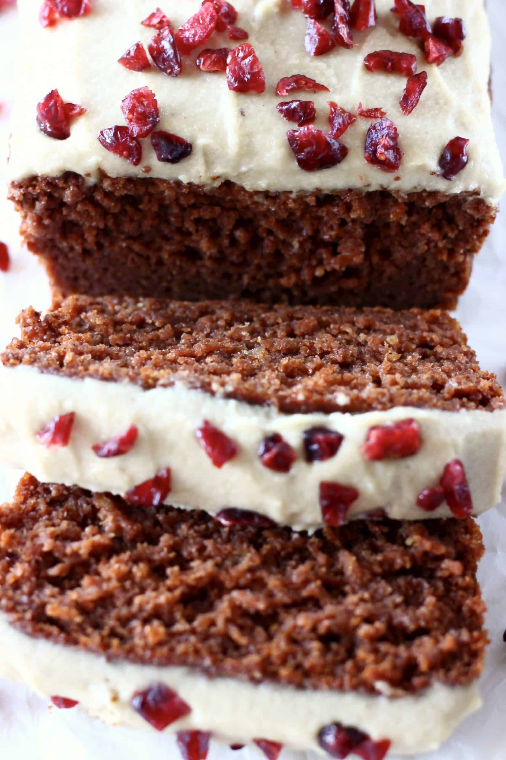 Gingerbread loaf cake topped with white frosting and dried cranberries with two slices next to it