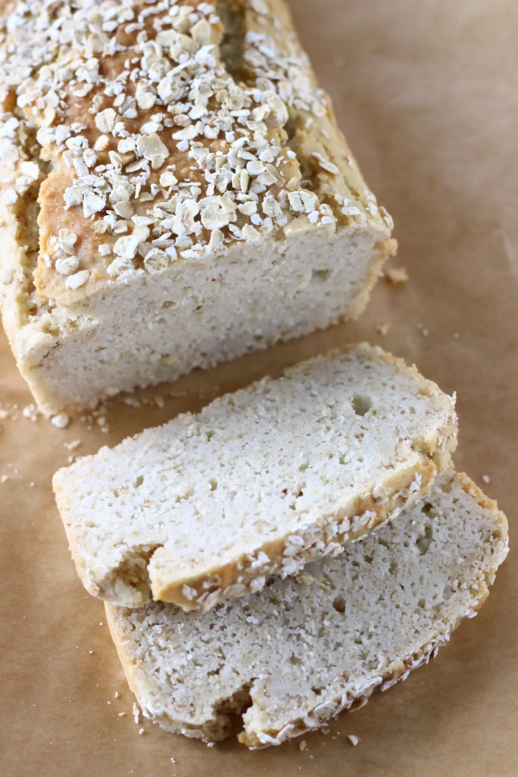 A loaf of gluten-free vegan oat bread topped with oats with two slices on the side