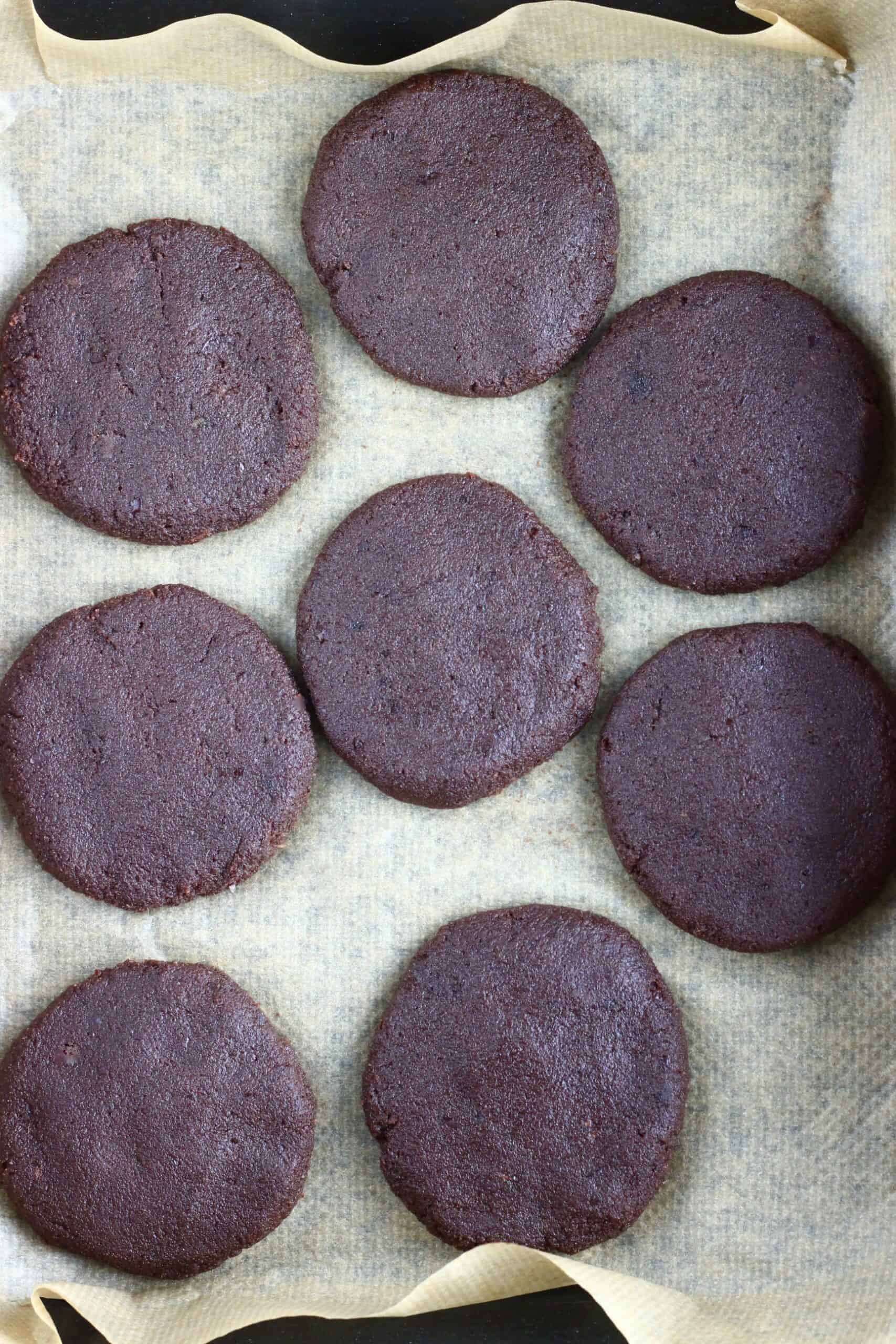 Eight raw gluten-free vegan chocolate brownie cookies on a baking tray lined with baking paper