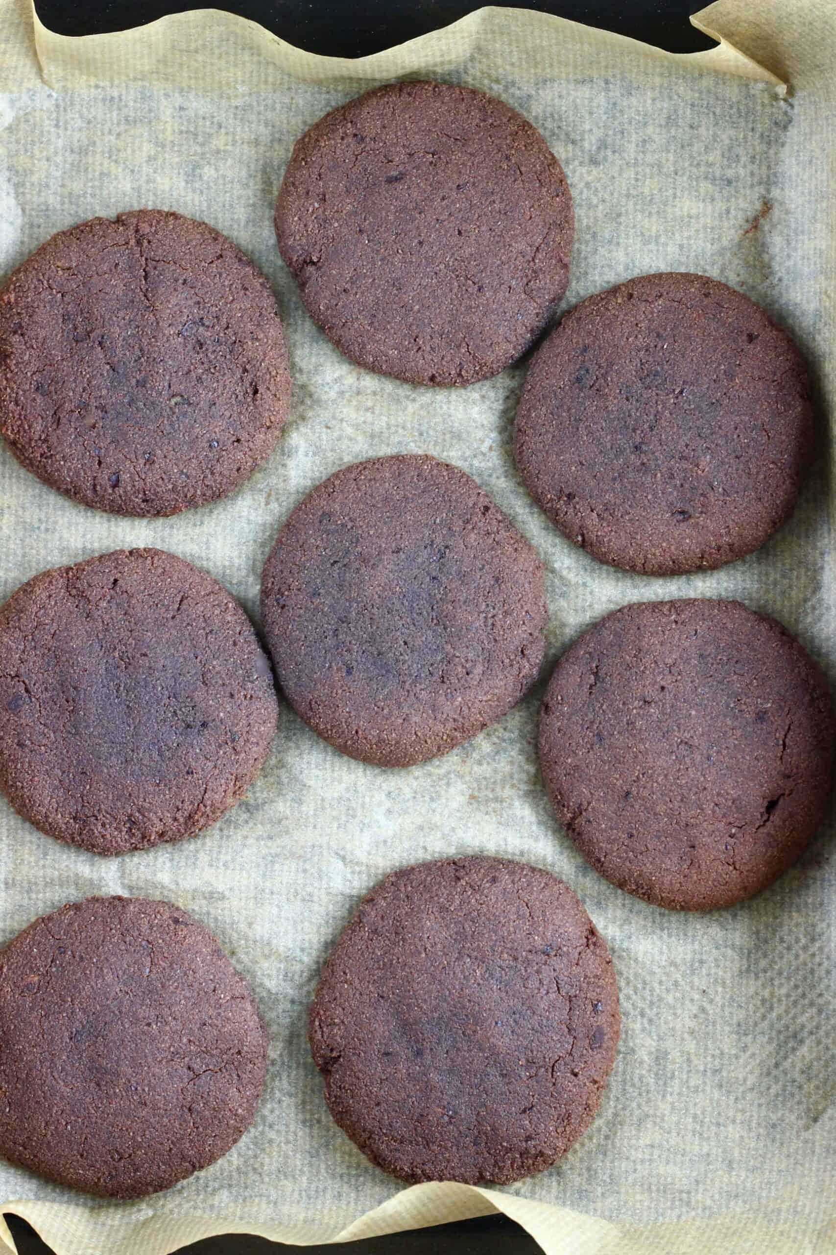 Eight gluten-free vegan chocolate brownie cookies on a baking tray lined with baking paper