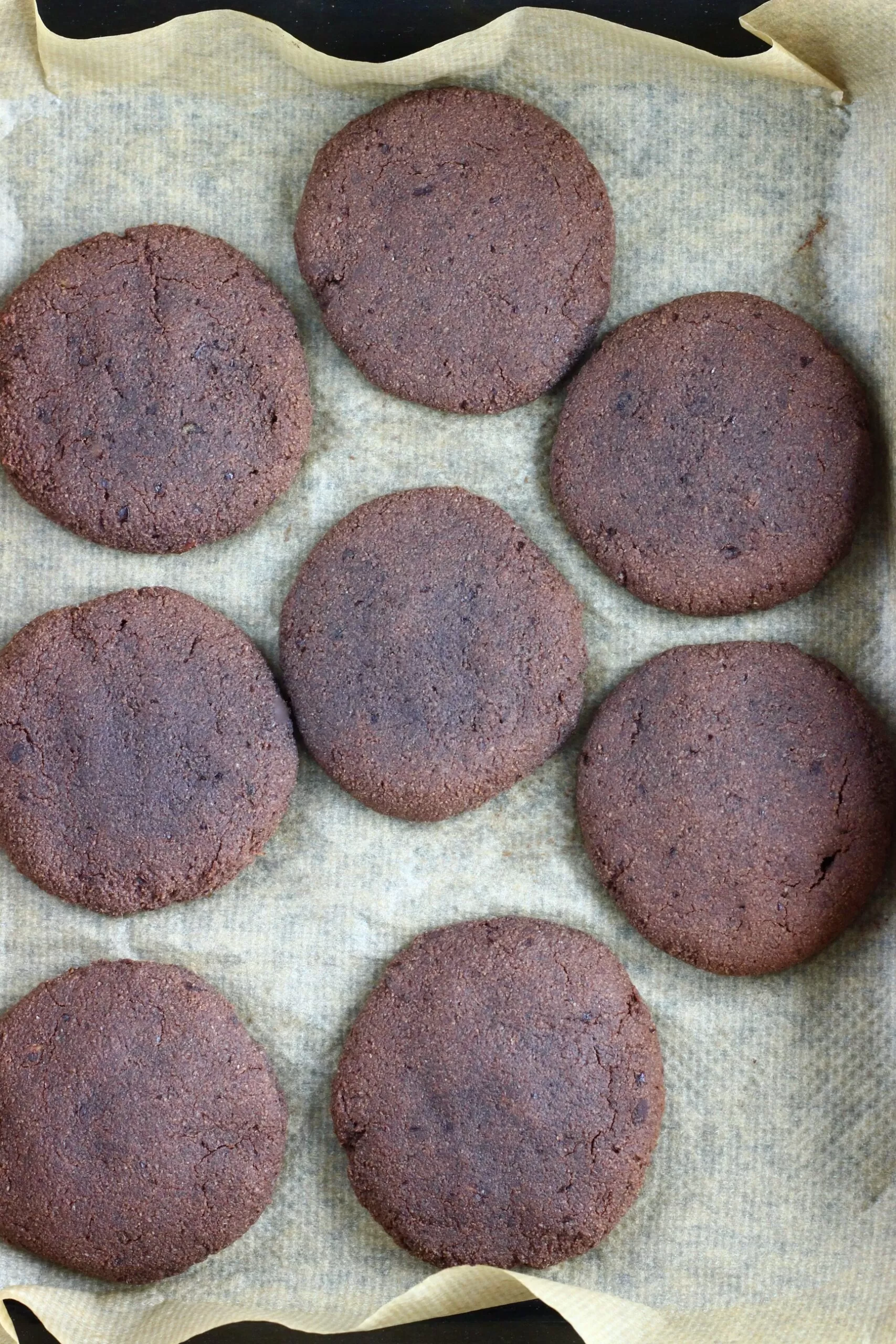 Eight gluten-free vegan chocolate brownie cookies on a baking tray lined with baking paper