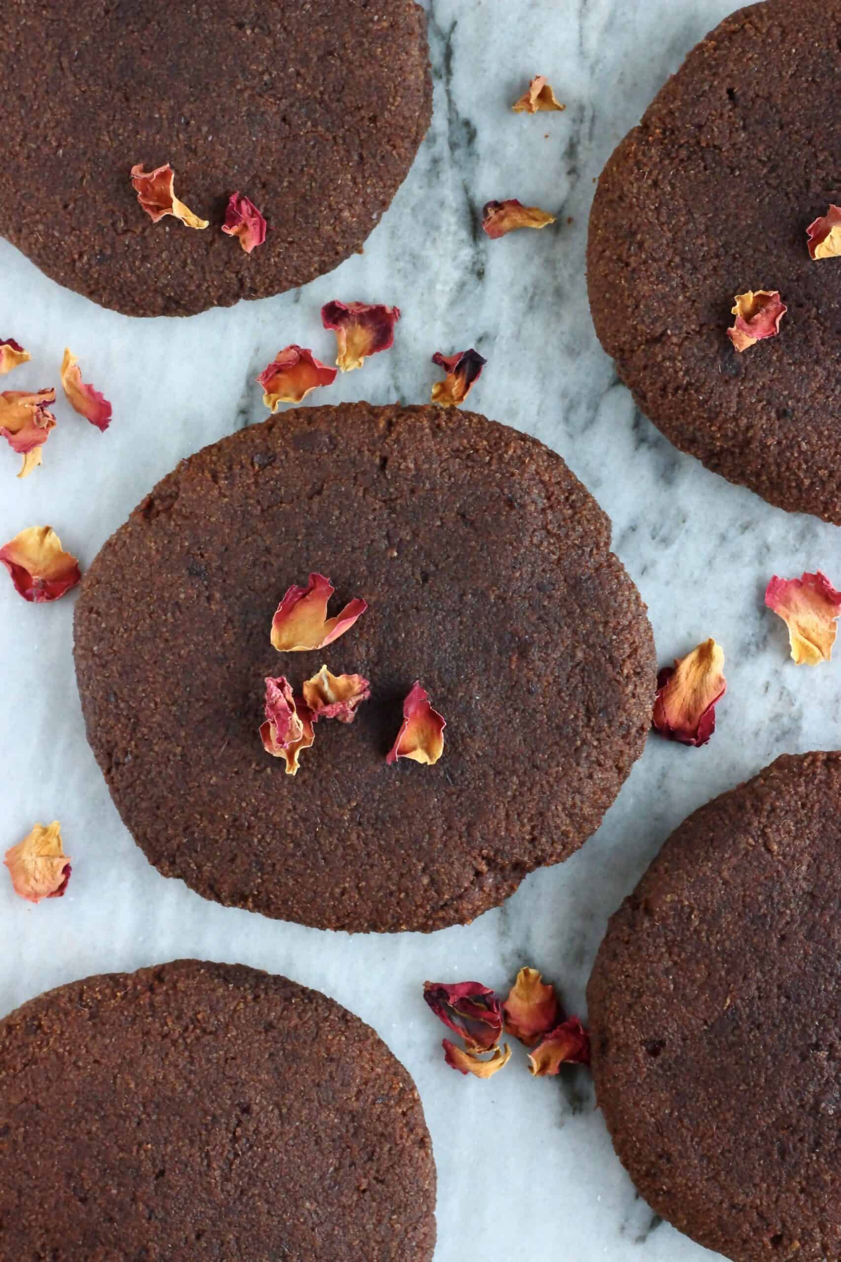 Five gluten-free vegan chocolate brownie cookies on a marble slab decorated with rose petals