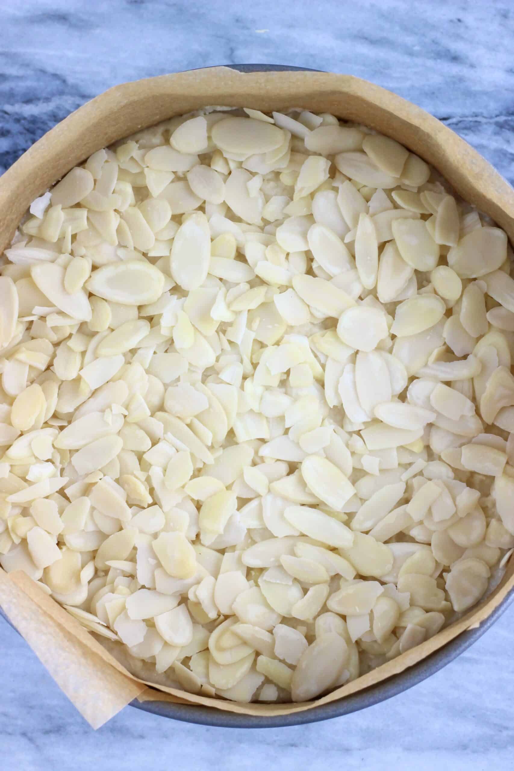 Raw gluten-free vegan almond cake batter topped with flaked almonds in a springform baking tin lined with baking paper