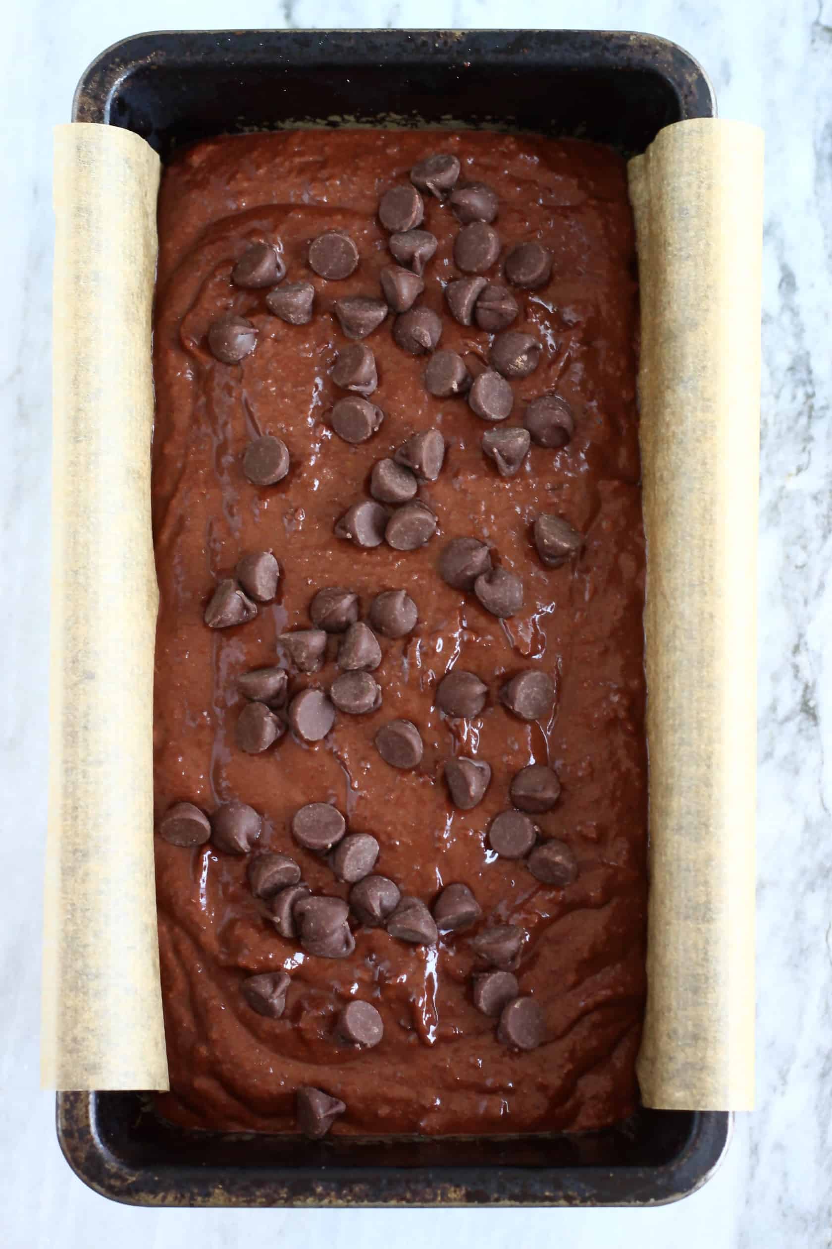 Gluten-free vegan chocolate bread batter with chocolate chips in a loaf tin lined with baking paper