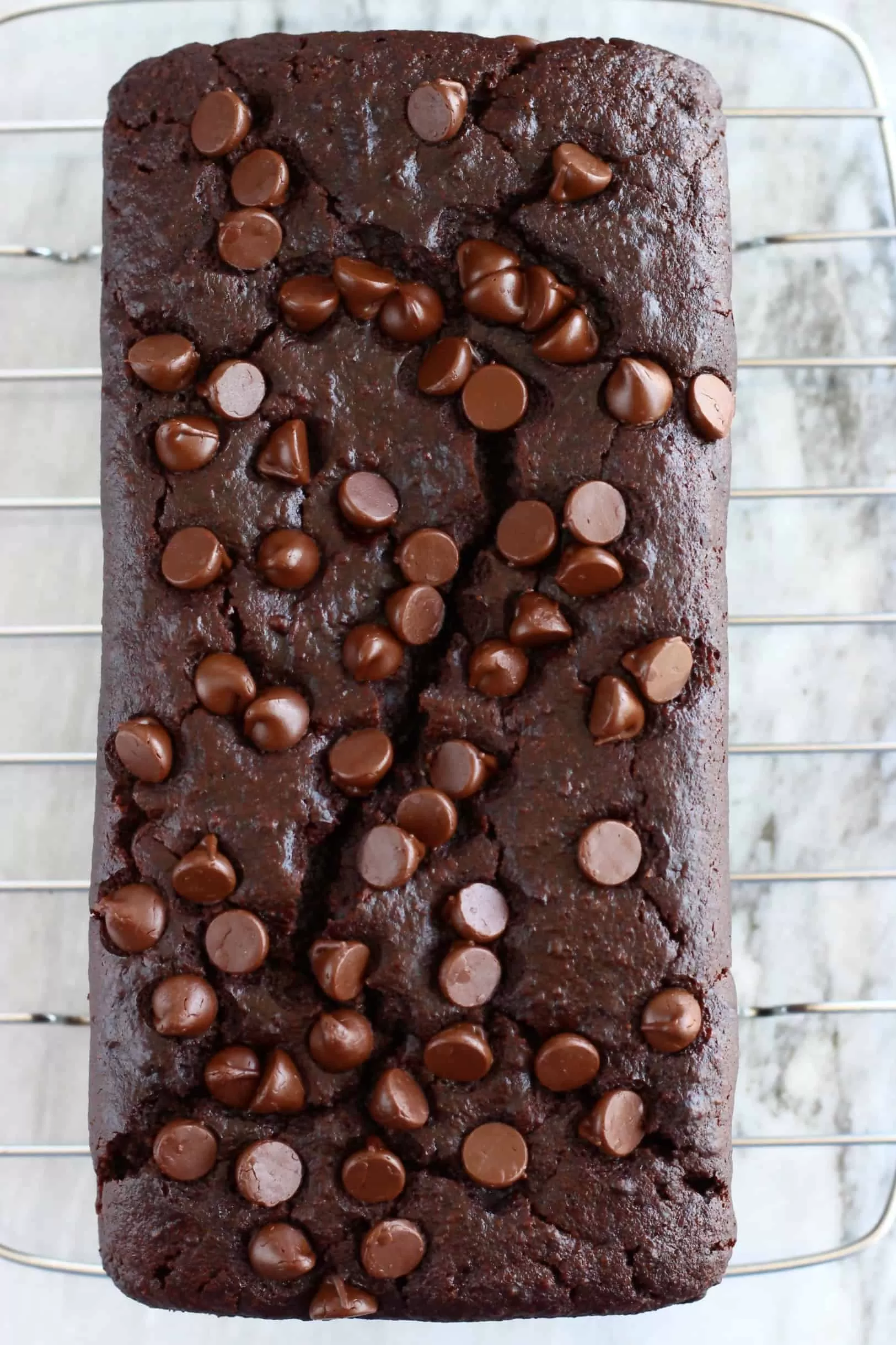 A loaf of gluten-free vegan chocolate bread topped with chocolate chips on a wire rack