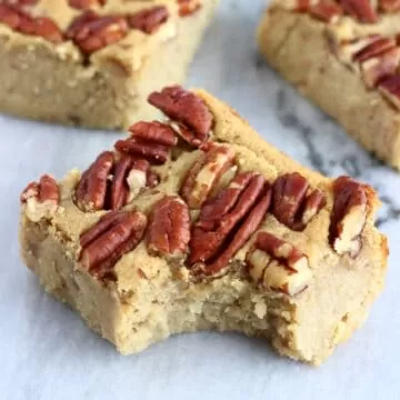 Three sweet potato blondies topped with pecan nuts with a bite taken out of one