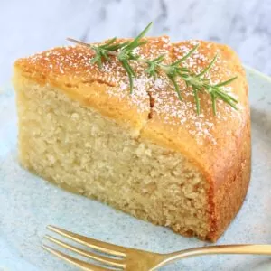 A slice of gluten-free vegan olive oil cake decorated with rosemary on a plate with a fork