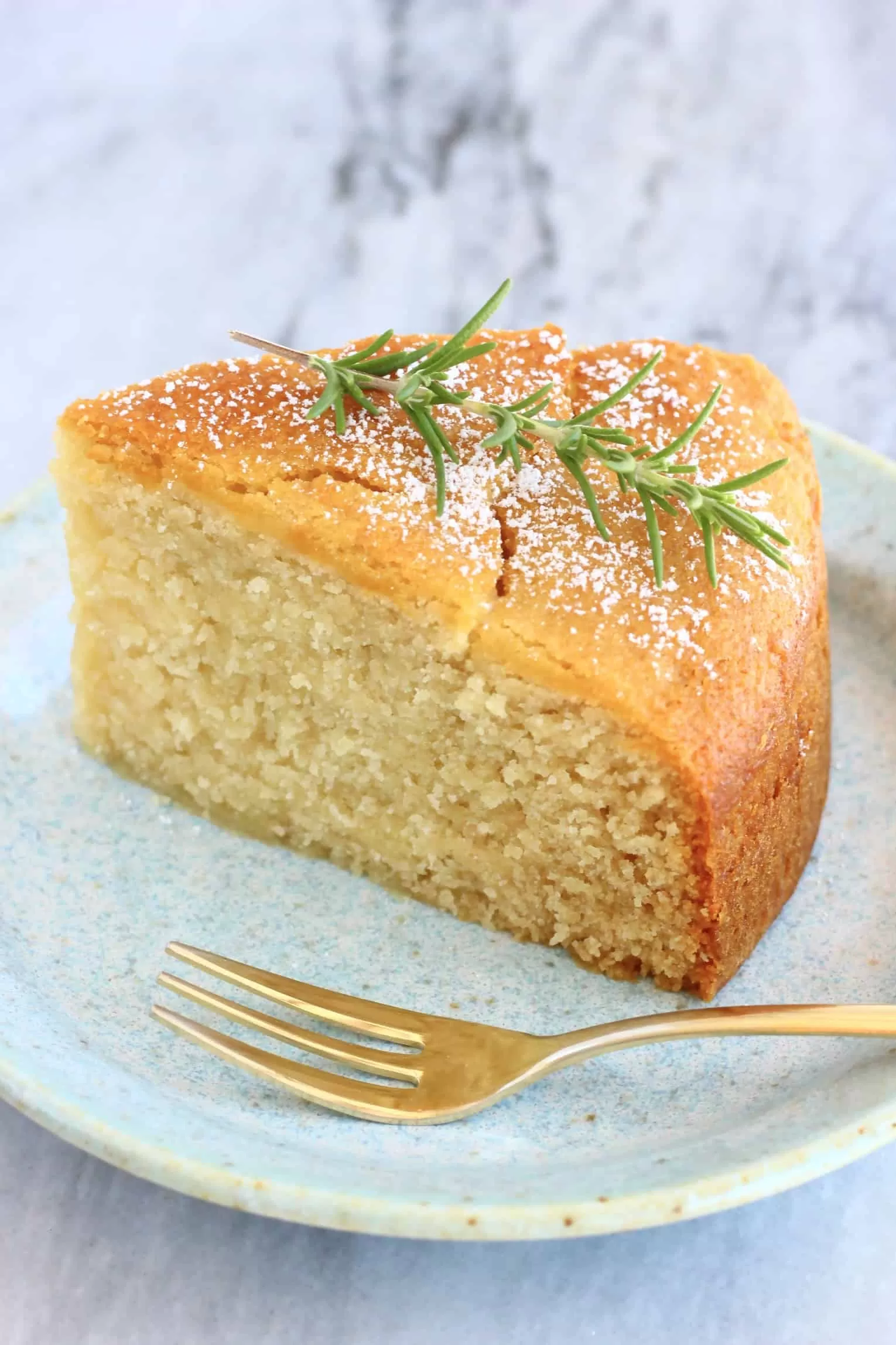 A slice of gluten-free vegan olive oil cake decorated with rosemary on a plate with a fork