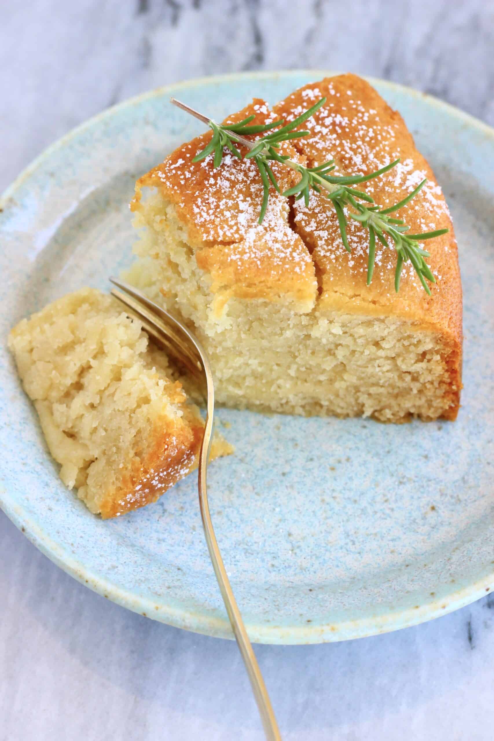 A slice of gluten-free vegan olive oil cake on a plate with a gold fork taking a bite out of it