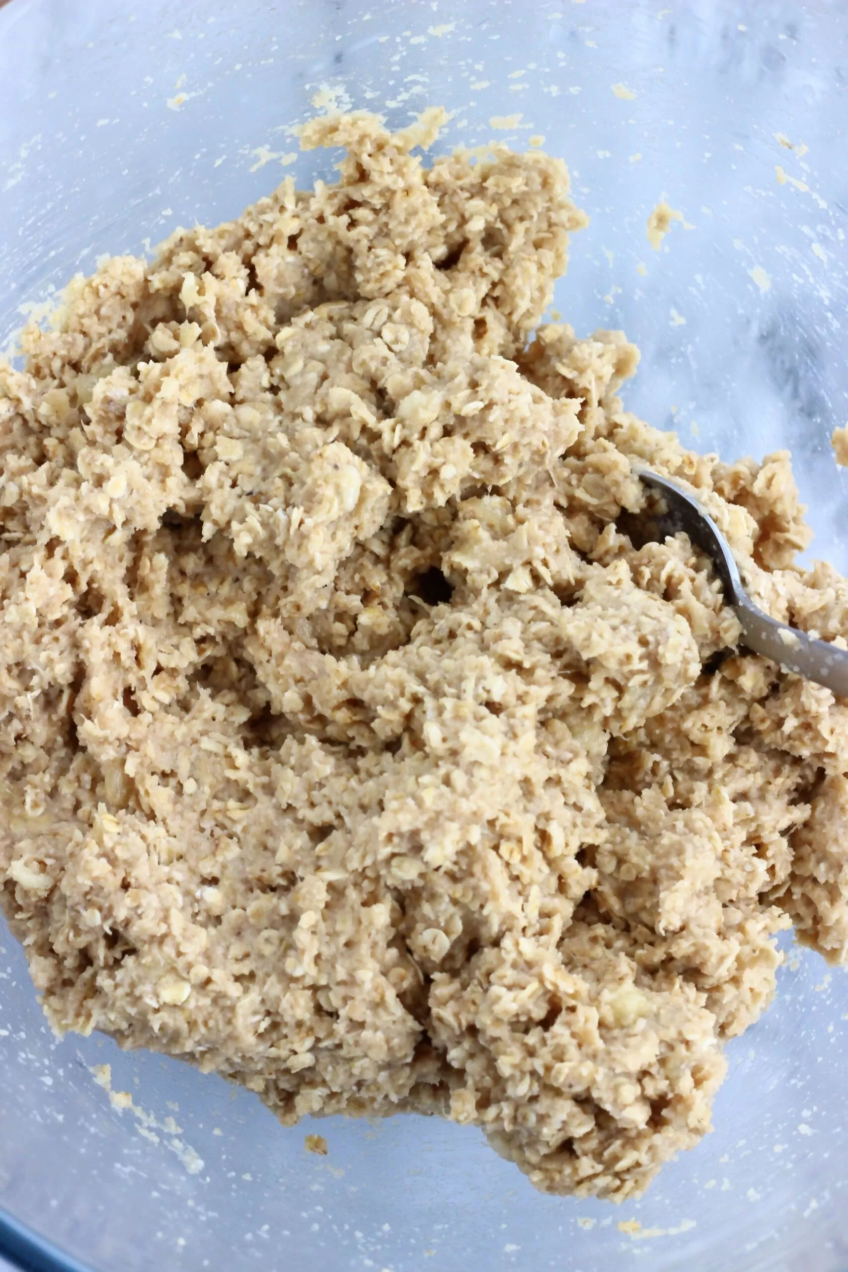 Raw baked banana oatmeal bars batter in a mixing bowl with a spoon