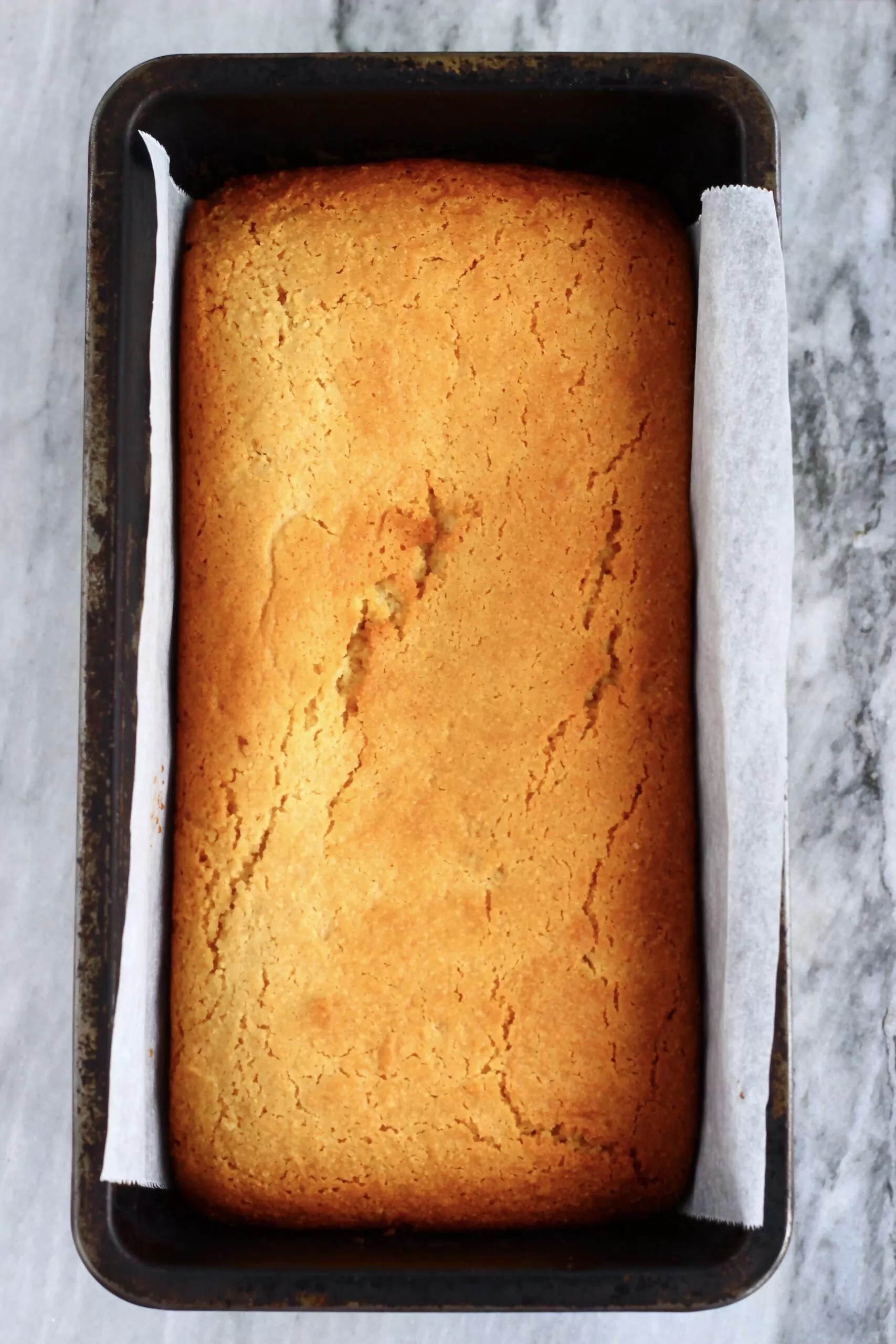 Vegan lemon drizzle loaf cake in a loaf tin lined with baking paper