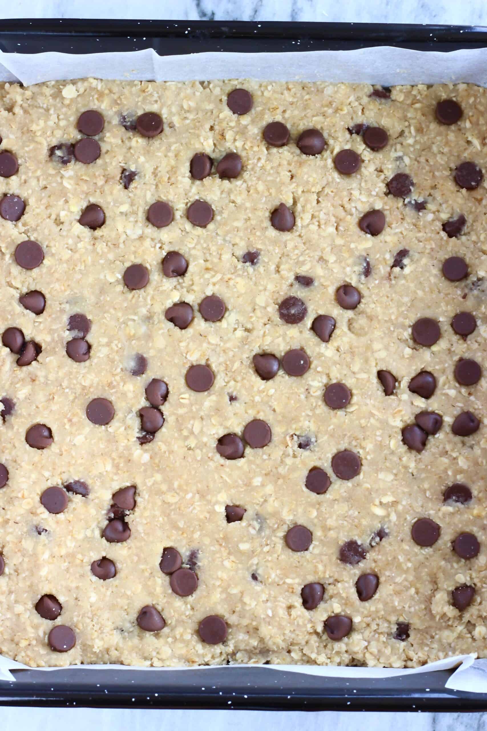 Raw gluten-free vegan oatmeal chocolate chip cookie bars batter in a square baking tin