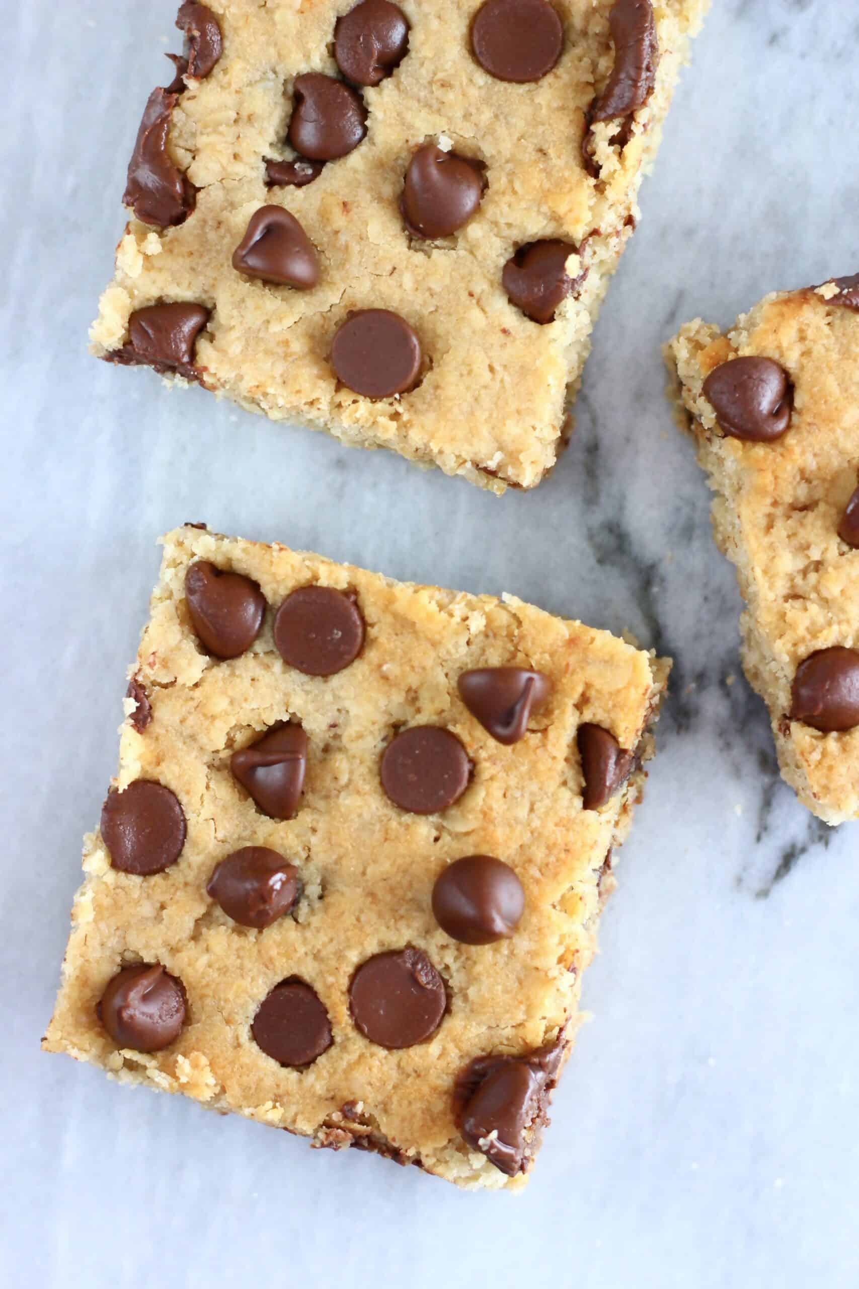Three gluten-free vegan oatmeal chocolate chip cookie bars on a marble background