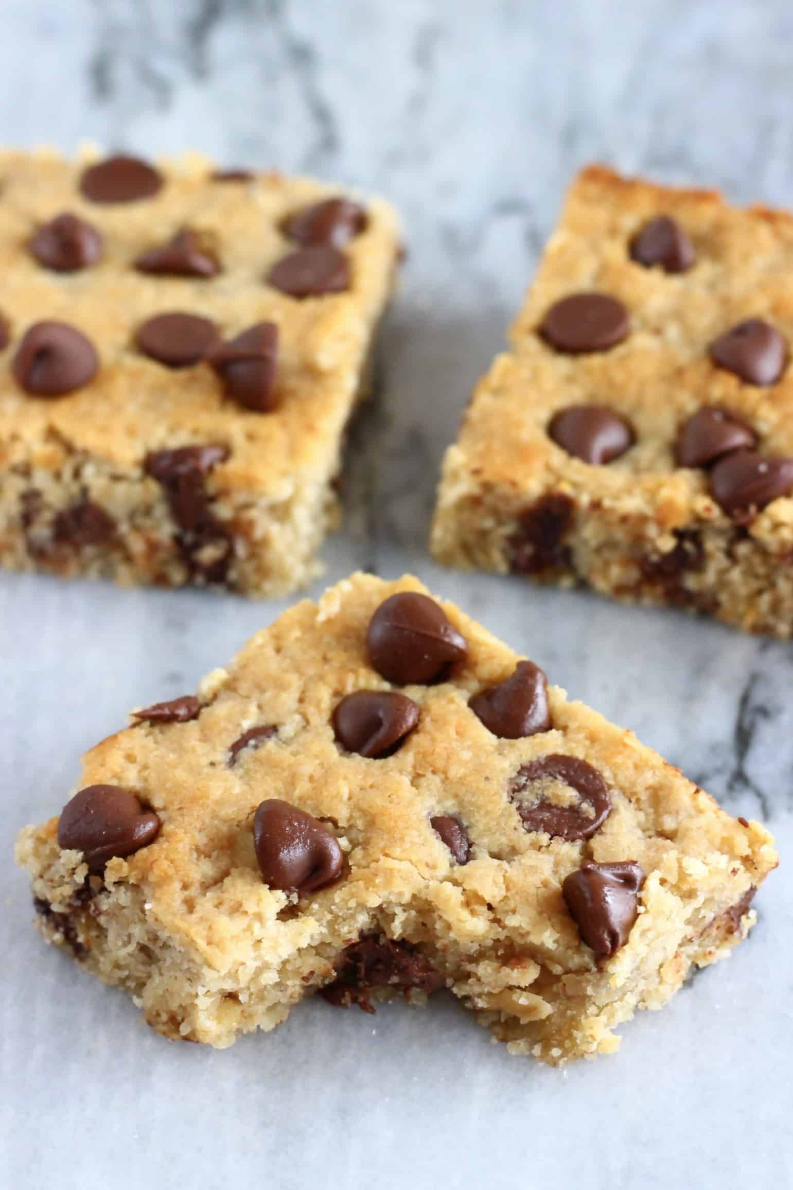 Three gluten-free vegan oatmeal chocolate chip cookie bars with a bite taken out of one