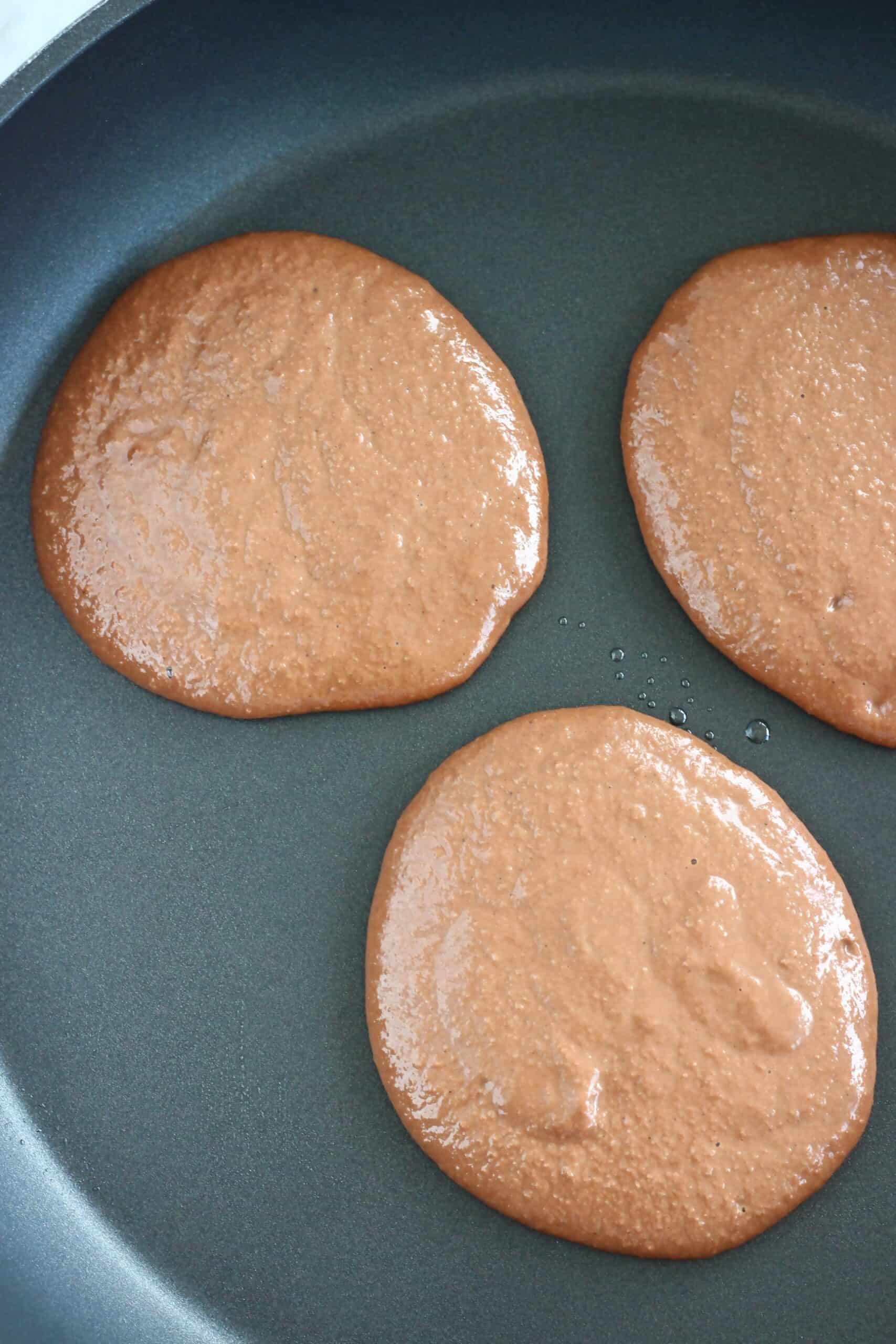 Raw gluten-free vegan chocolate pancakes being cooked in a frying pan